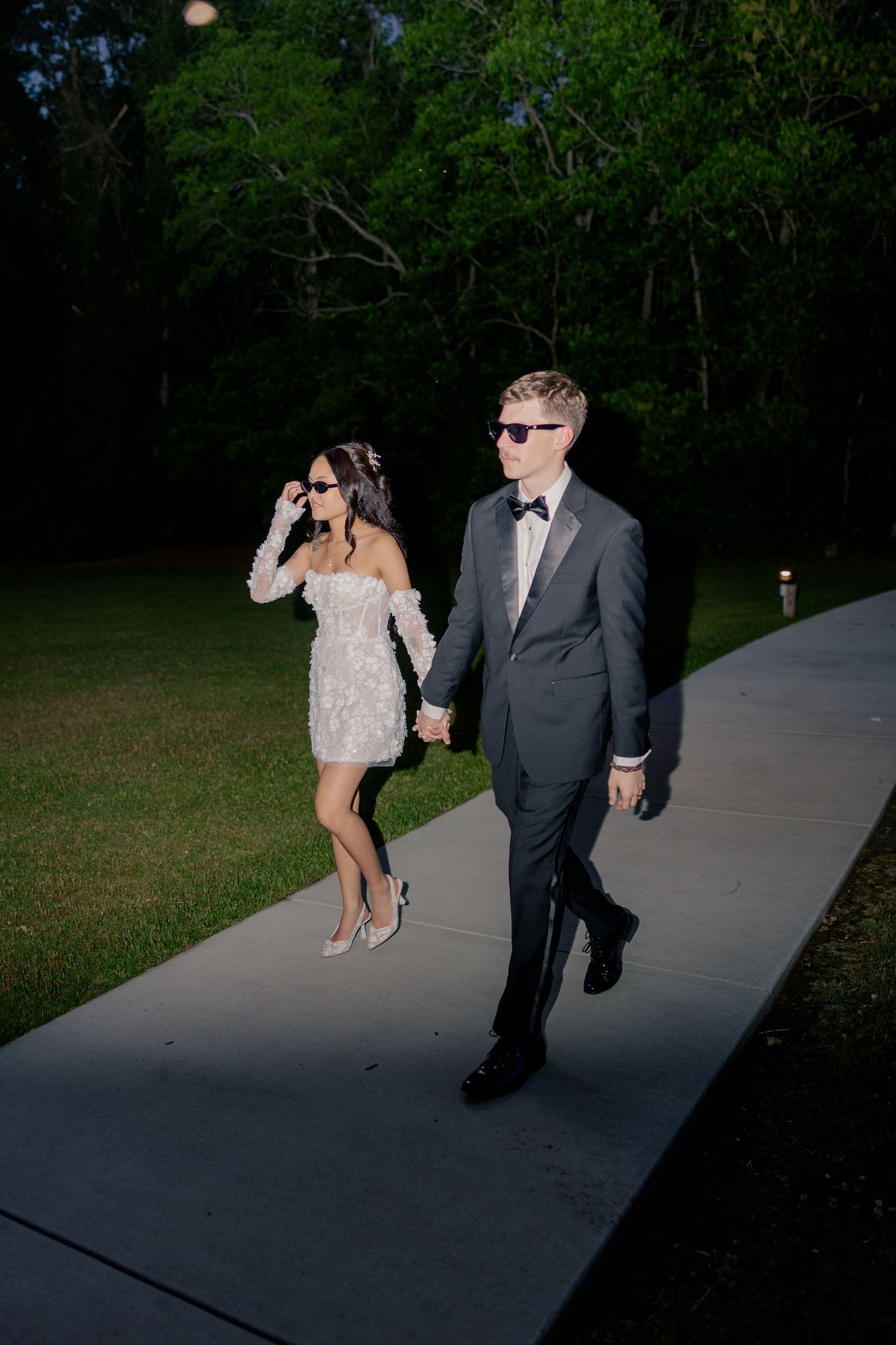 Evening wedding photo of couple walking on illuminated pathway.