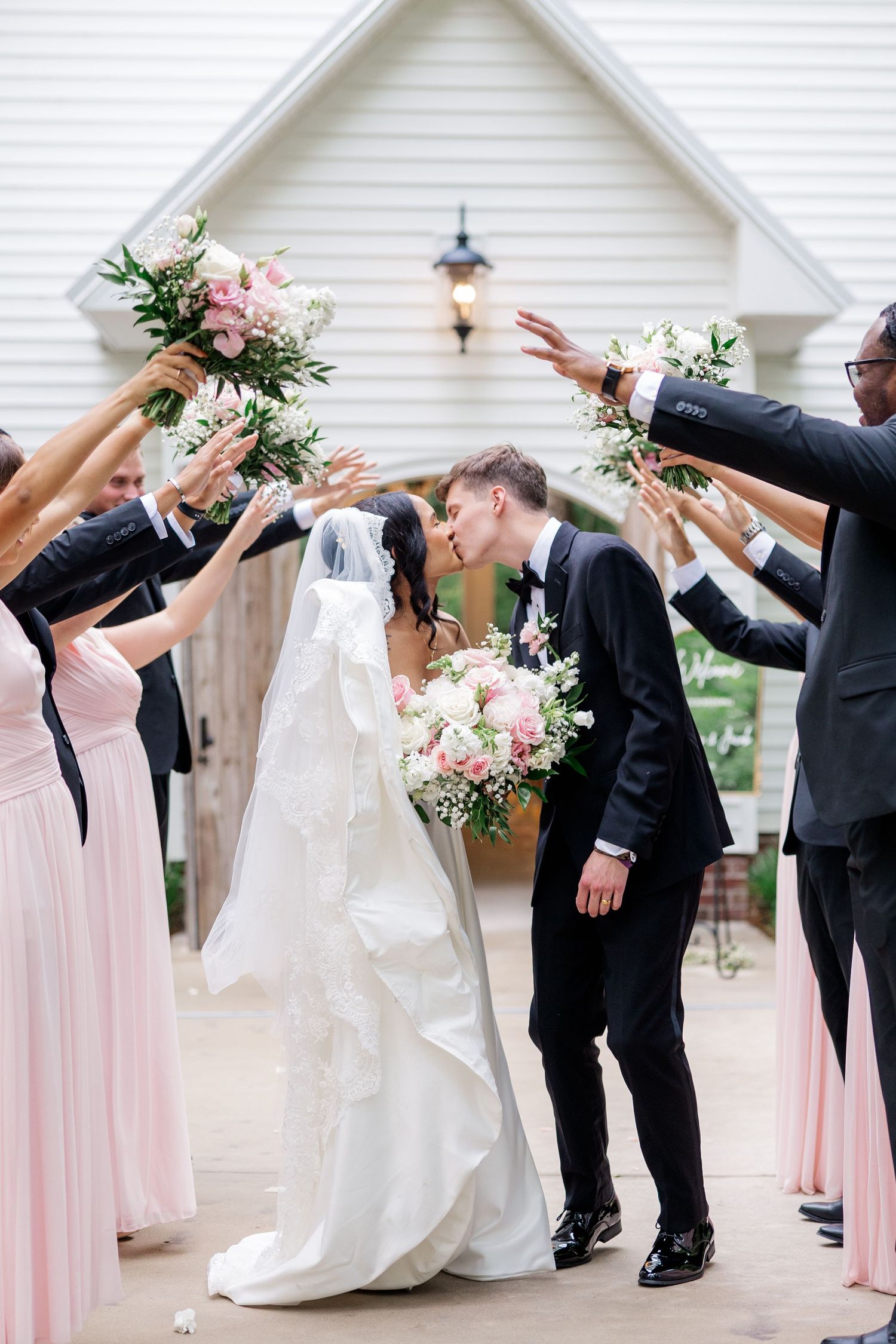 Wedding party forms a celebratory tunnel with arms raised for the newlyweds.