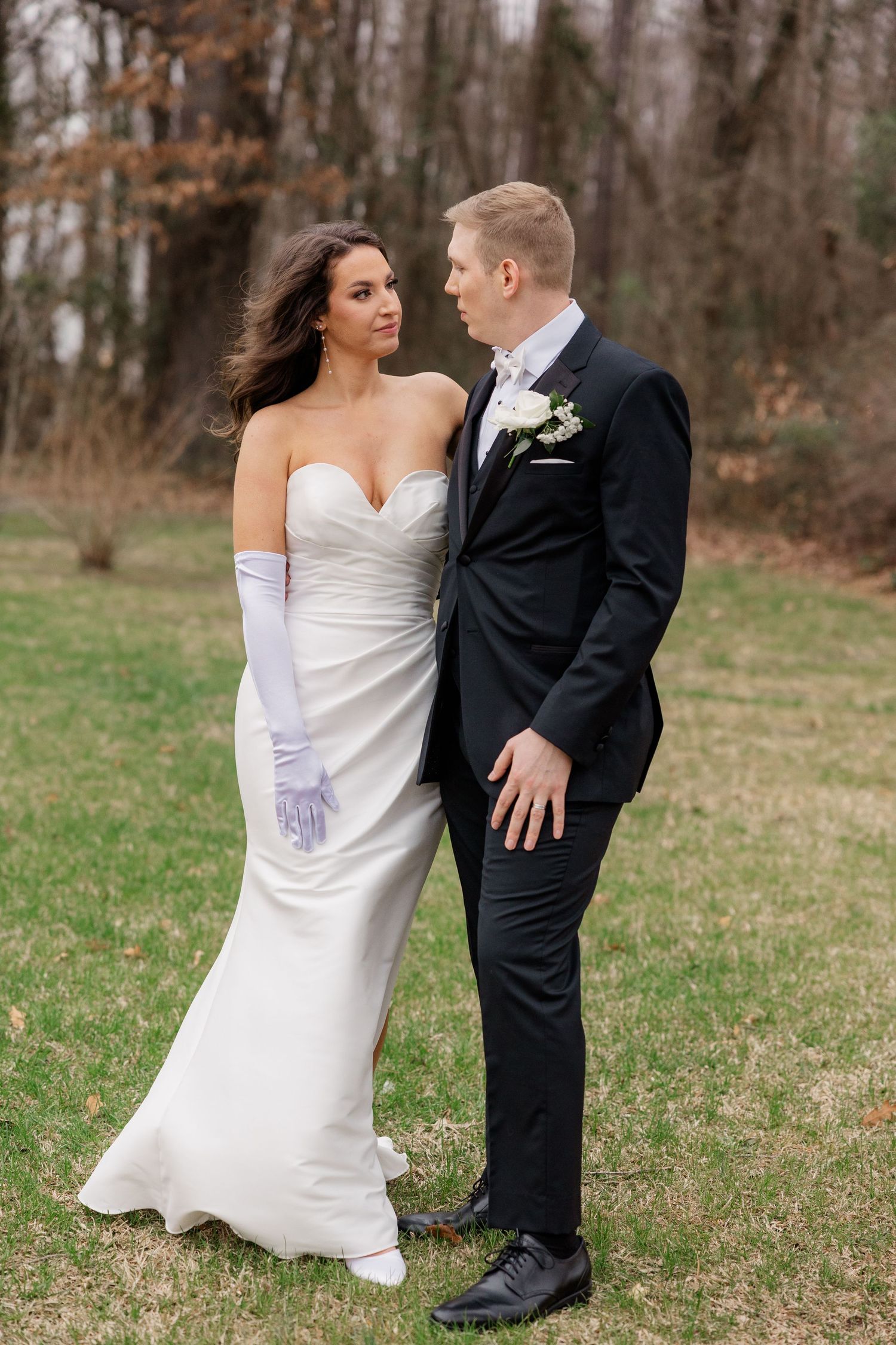 Newlyweds pose playfully on grass with bride's dress flowing in elegant outdoor wedding photos.