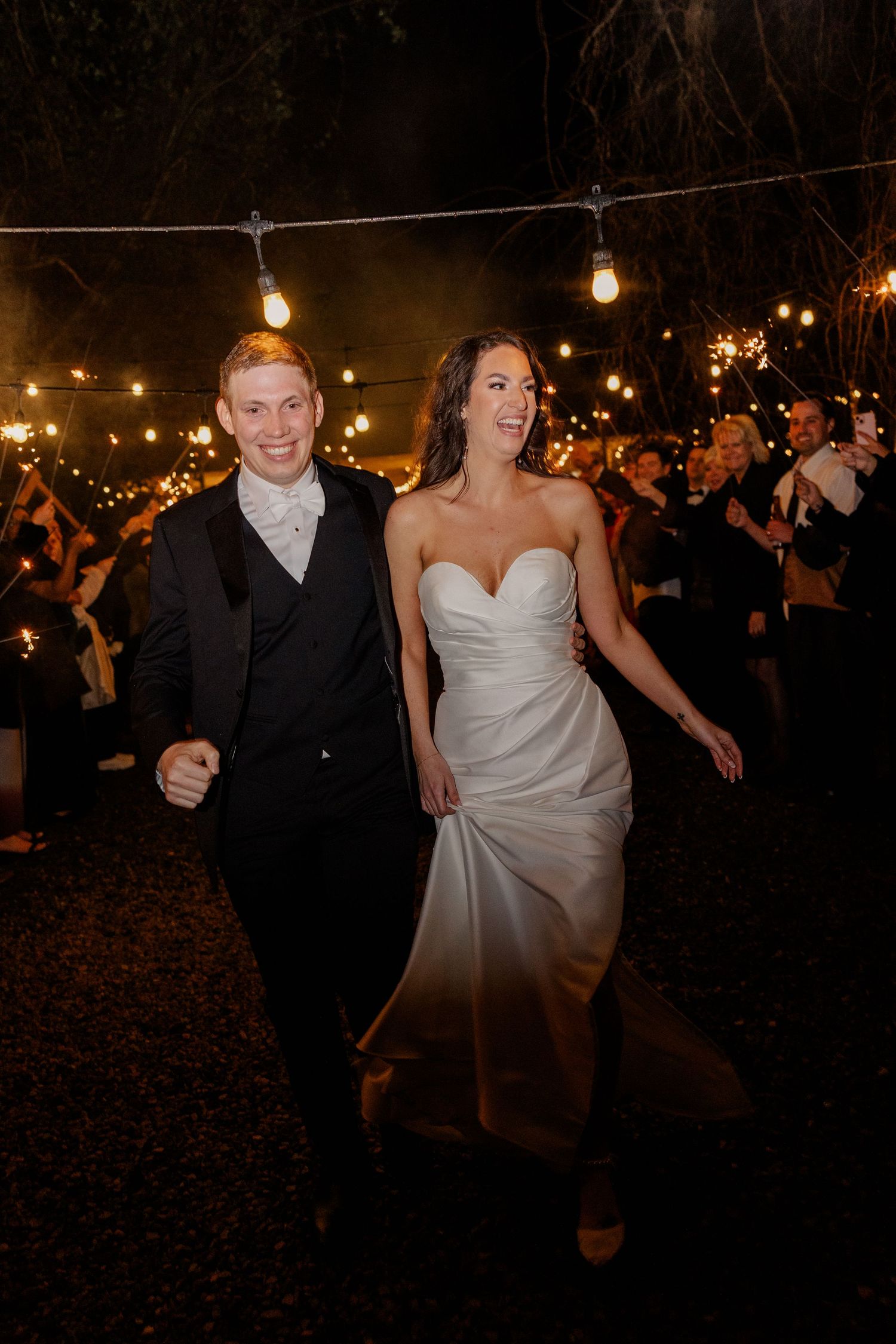 Outdoor nighttime wedding celebration with string lights illuminating dancing guests.