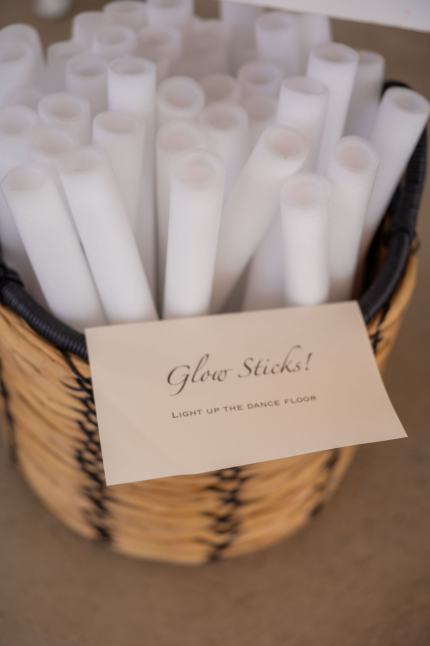 White glow sticks arranged in a decorative basket with an event label for wedding festivities.