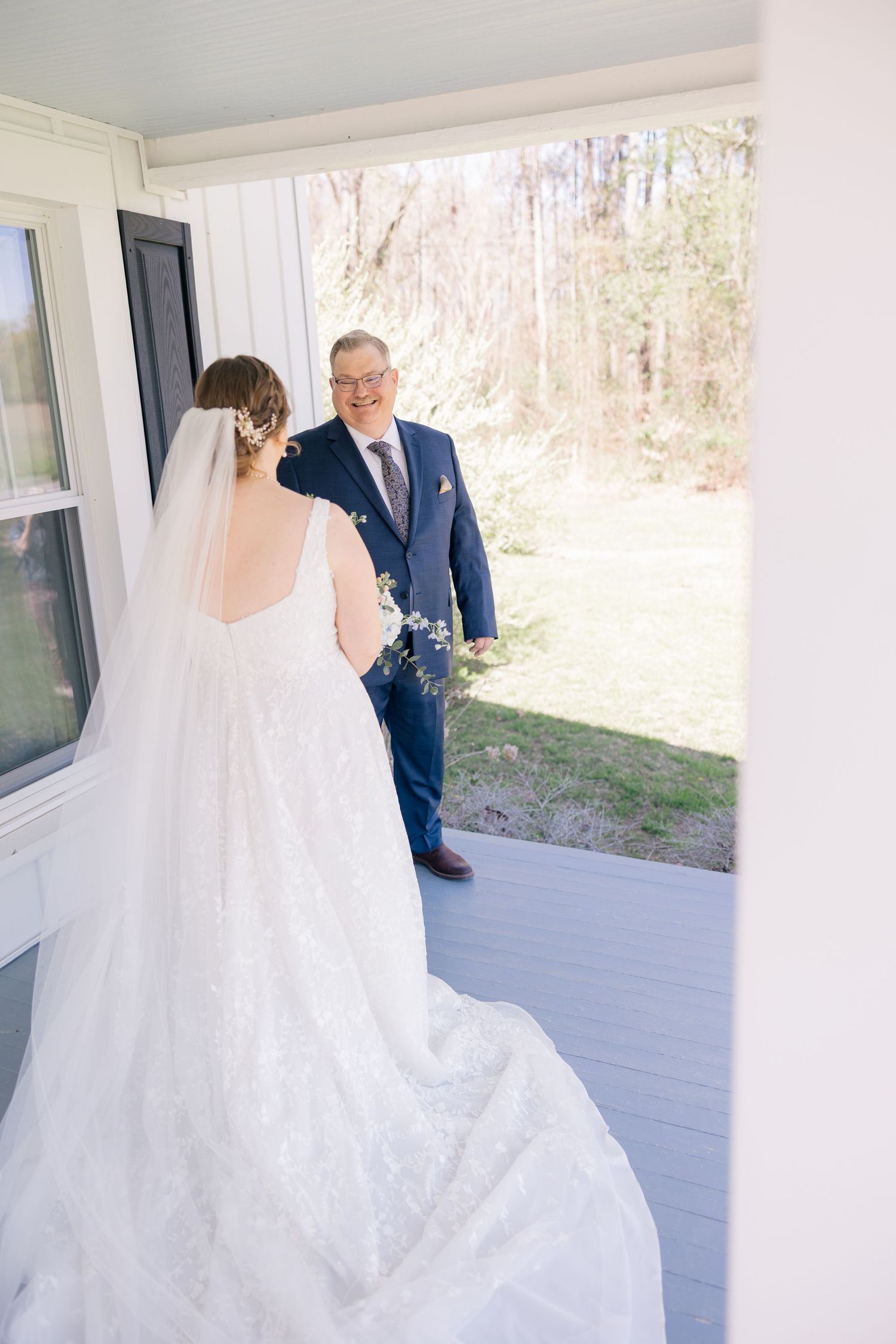 Bride in flowing white gown twirling on a covered porch with natural light streaming in.