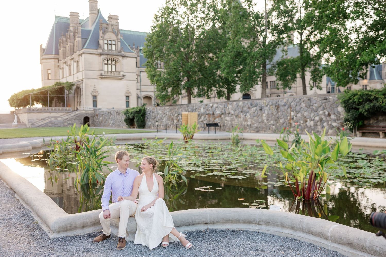 Biltmore House Photographer. A couple sits by a lily pond at sunset with a grand French chateau in the background.