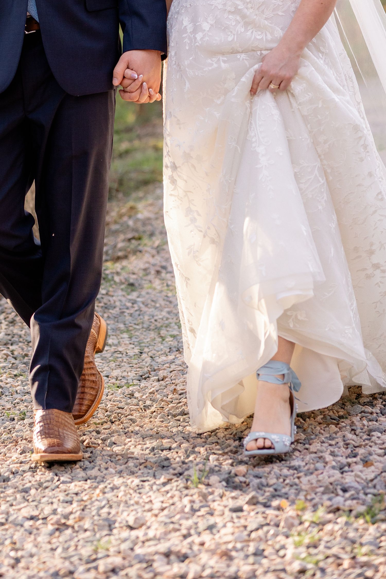 Close-up of bride and groom's feet walking together, showing dress hem, blue suit, and brown leather shoes.