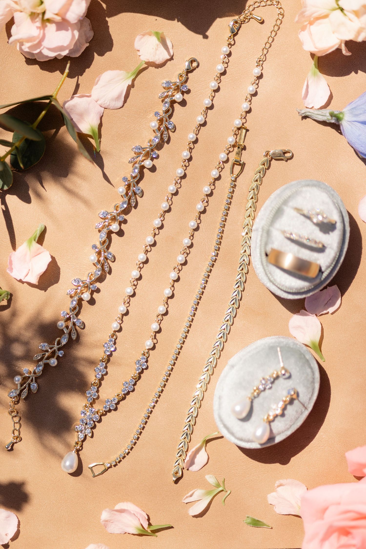 Wedding details with delicate crystal necklaces and rose petals arranged on a beige background.