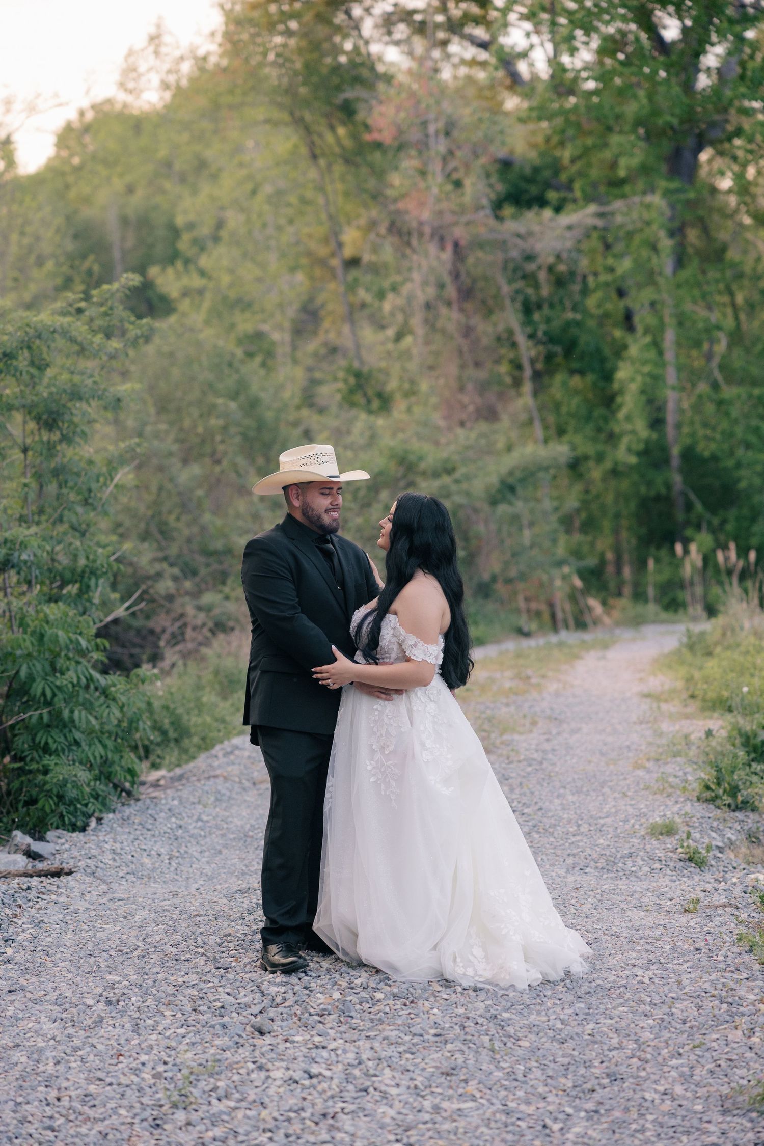 A romantic moment between newlyweds on a gravel path, with the groom wearing a western hat.
