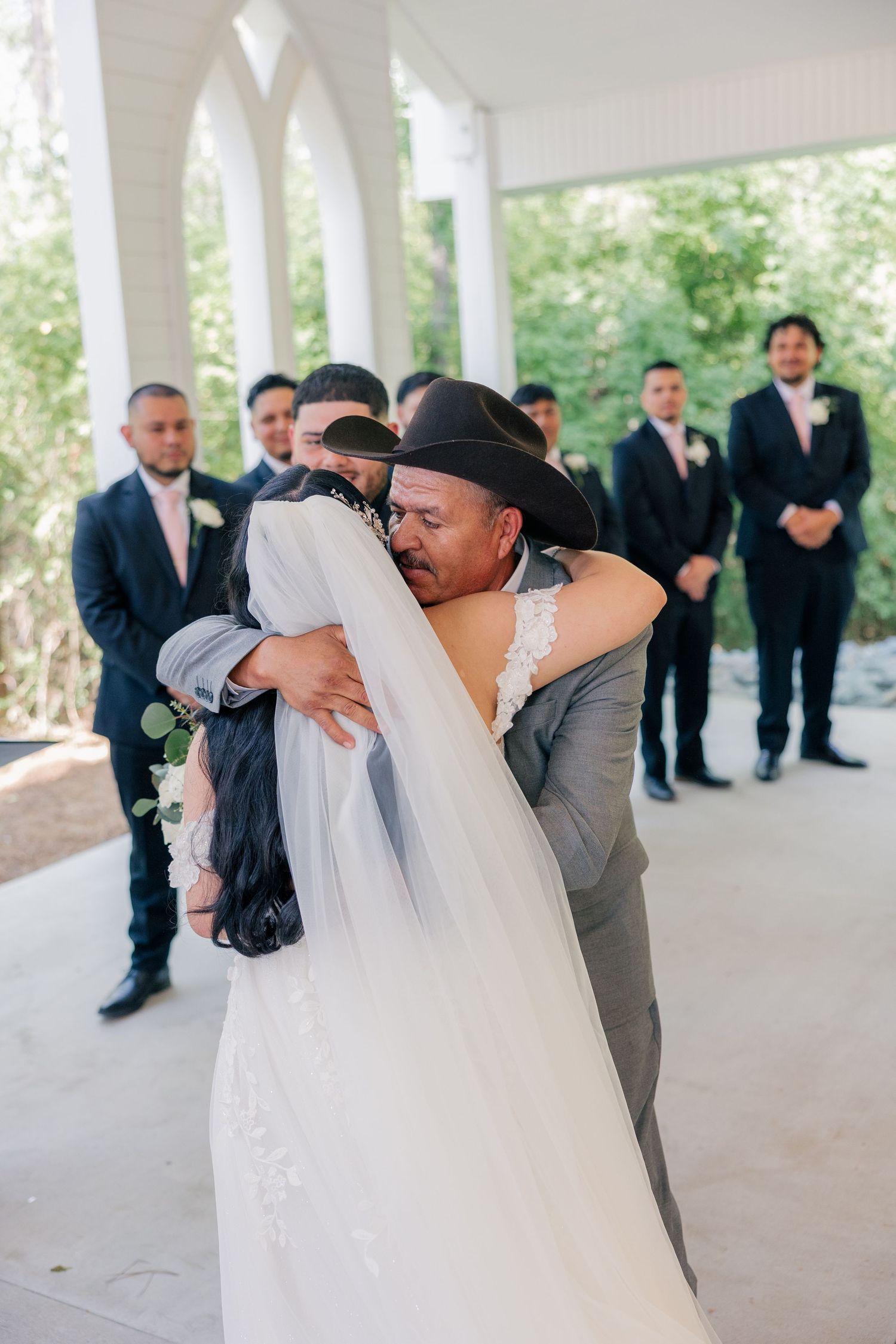 A couple embraces during their wedding ceremony while groomsmen look on in the background.