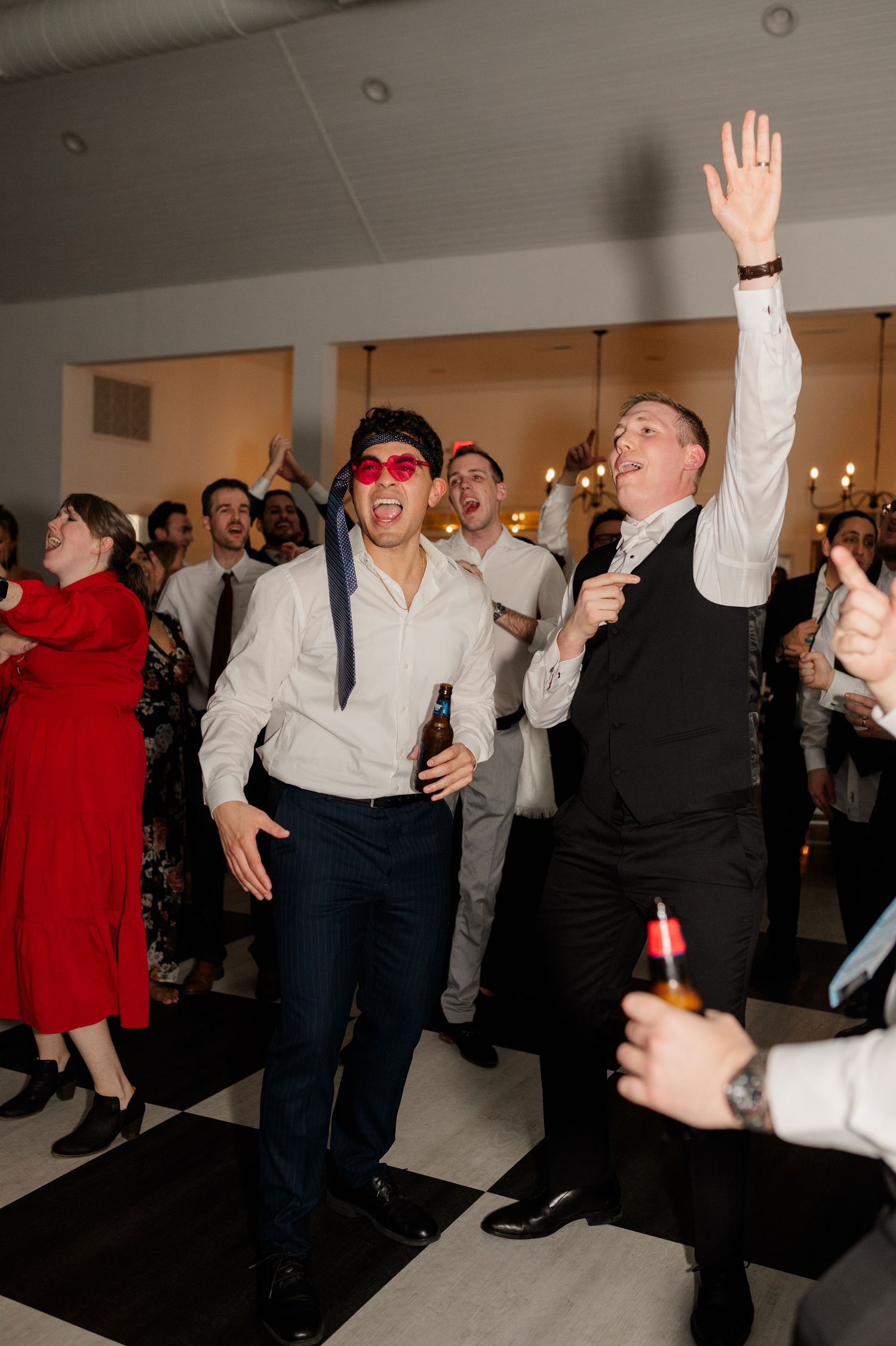 Wedding party guests dancing energetically at an indoor reception celebration.