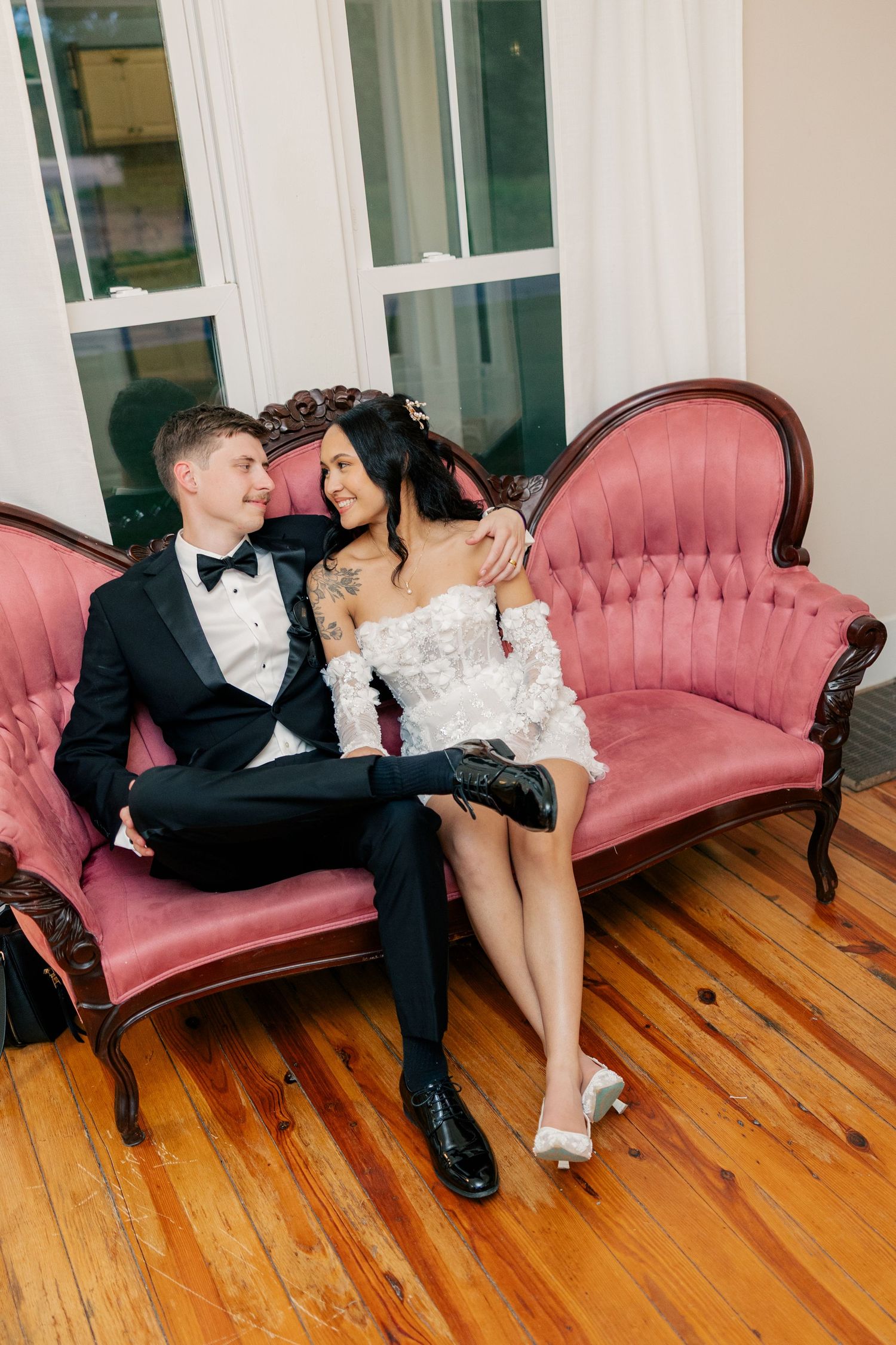 A romantic moment between newlyweds sitting on a vintage pink velvet couch.