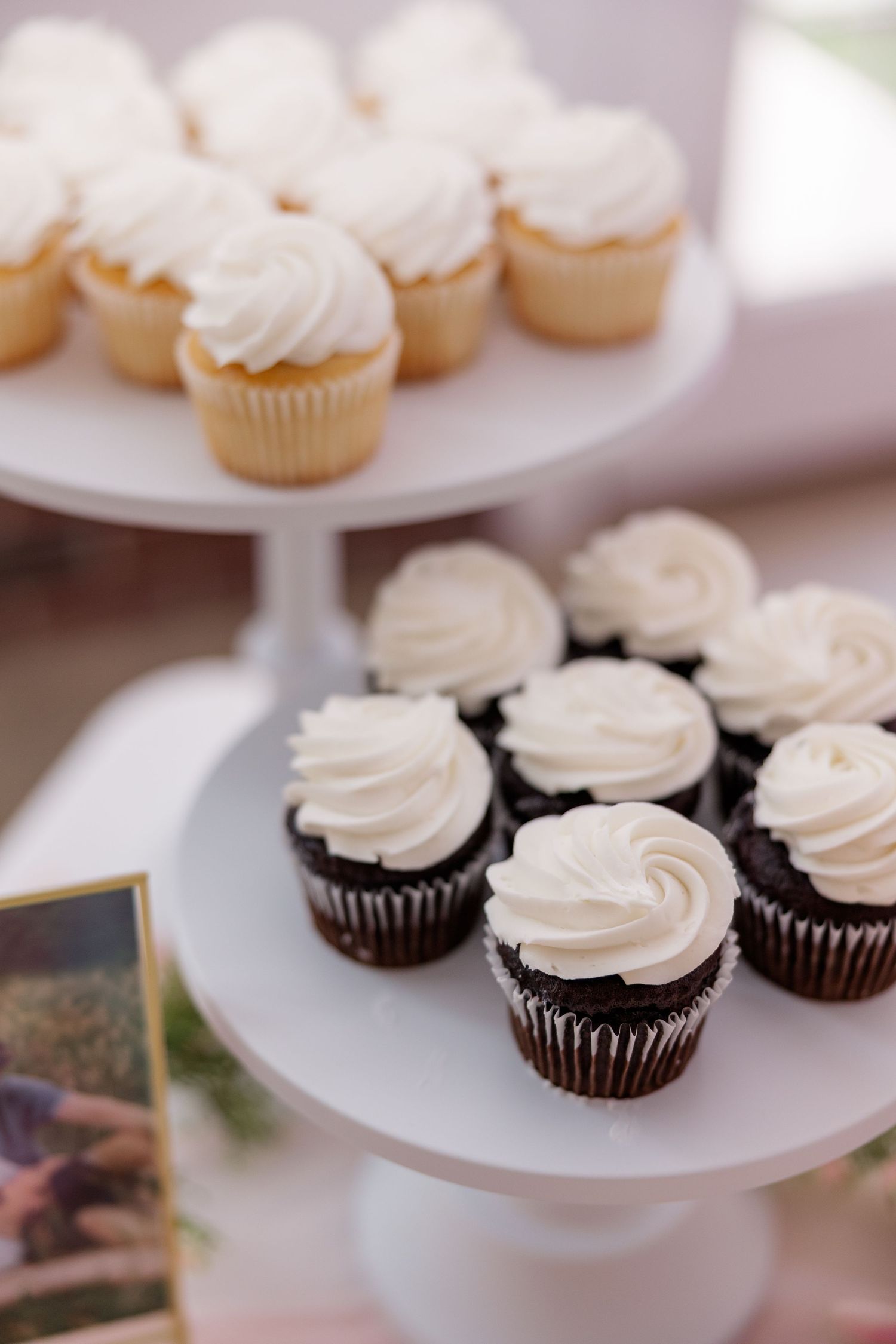 Two-tiered display of vanilla and chocolate cupcakes with swirled frosting.