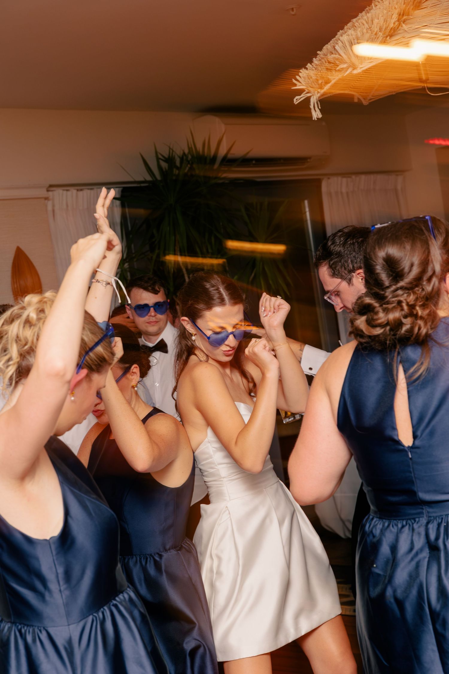 Bride and wedding guests dancing and celebrating on the dance floor wearing fun sunglasses.