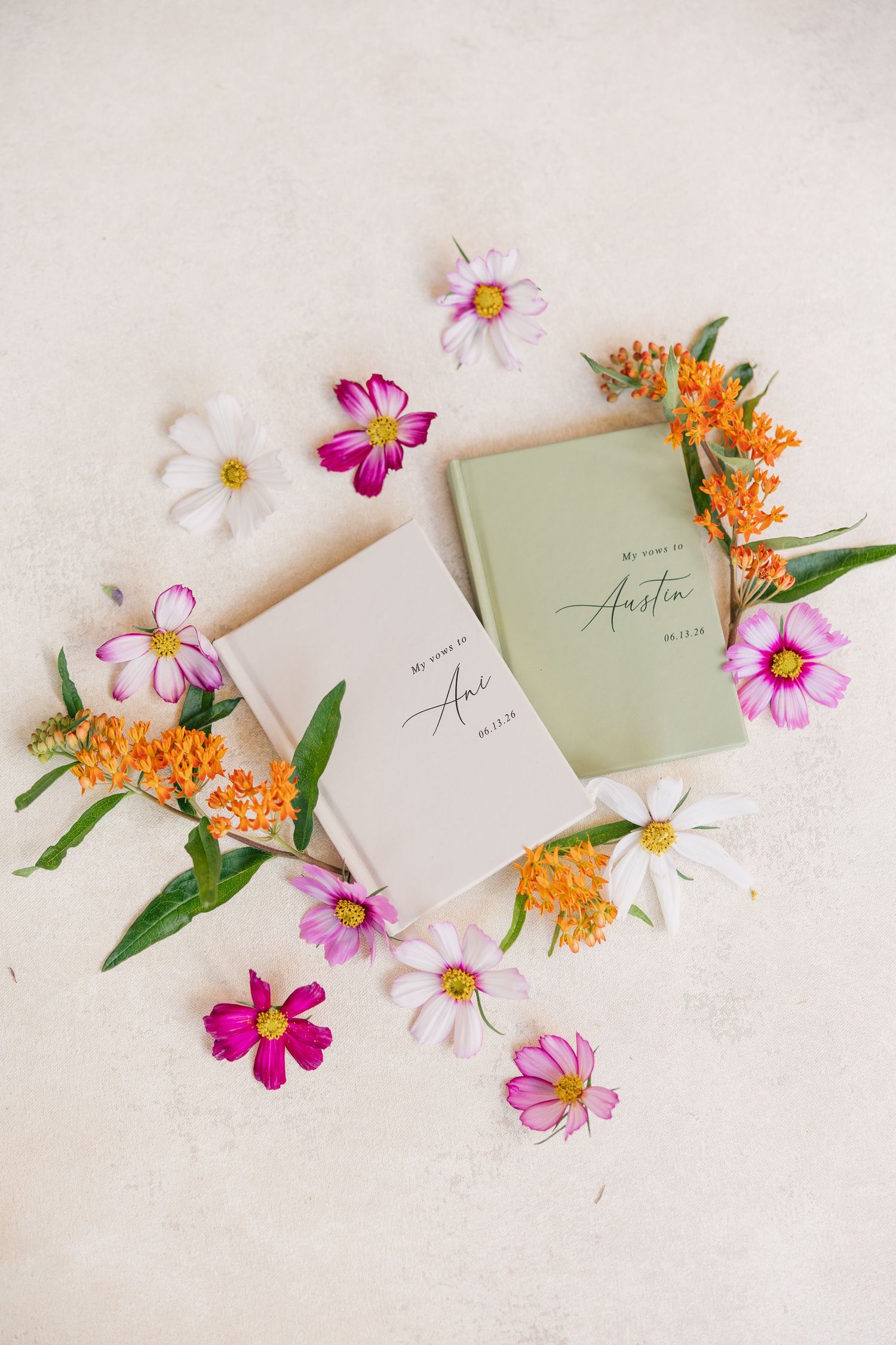 Wedding vow books for Ana and Austin surrounded by colorful pink, white, and orange wildflowers on a cream background.