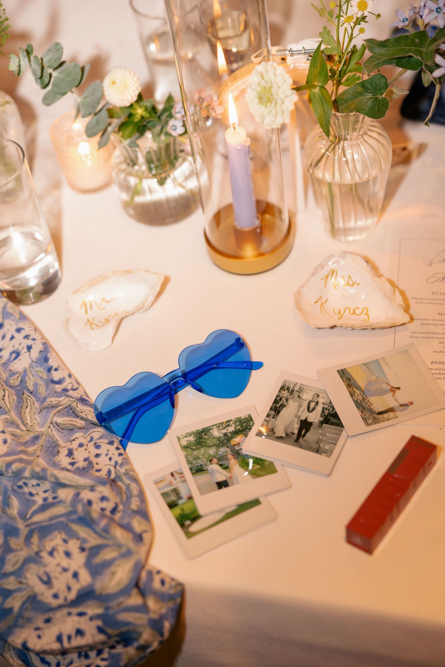Wedding reception table detail with blue heart sunglasses, Polaroid photos, and candles.