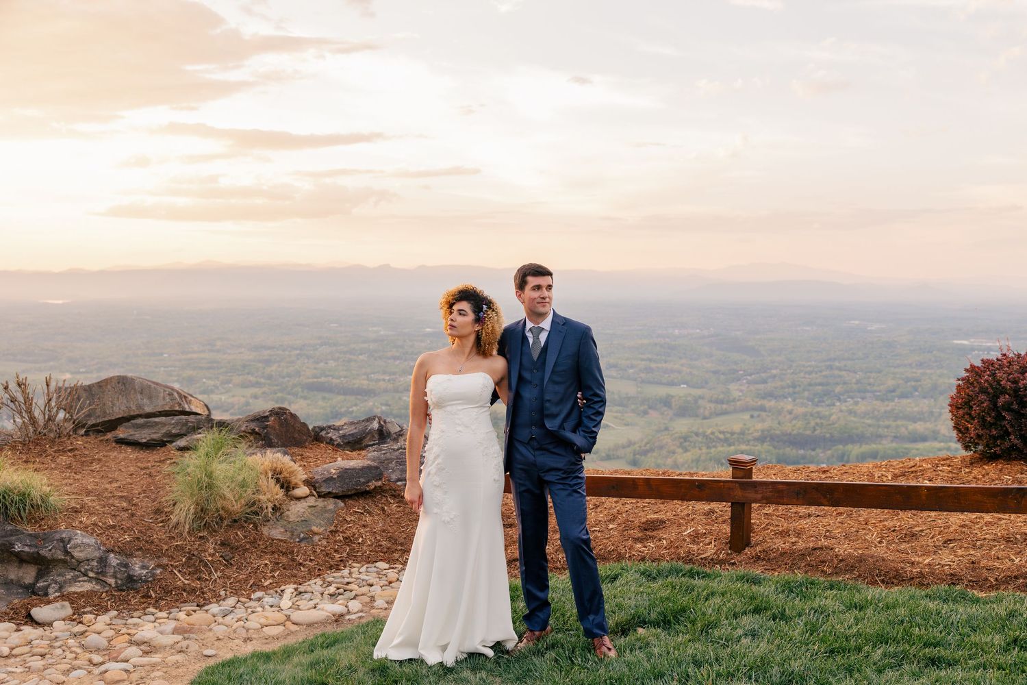 Bride and groom pose together at a scenic mountain overlook during golden hour sunset at their outdoor wedding.
