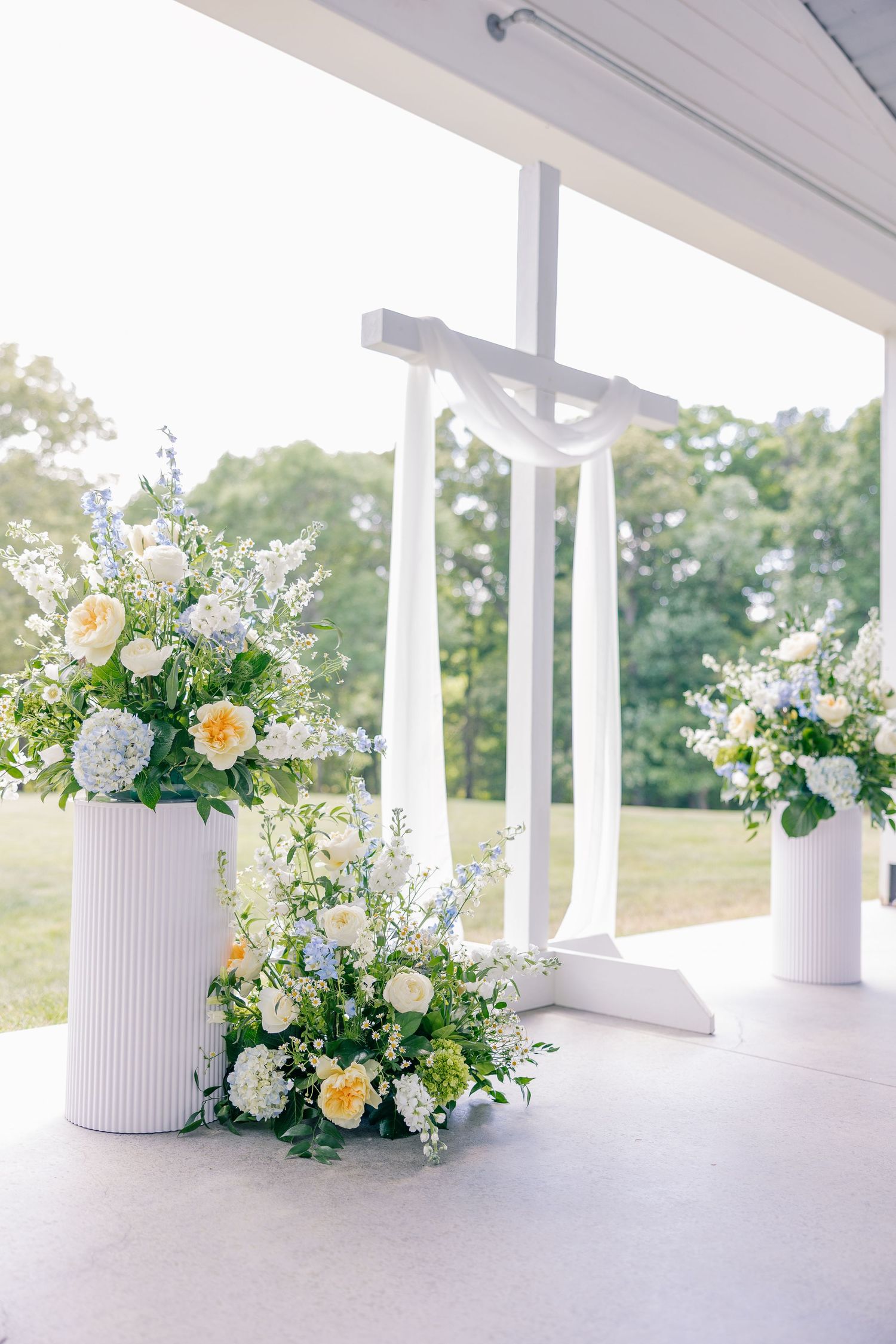 White cross altar decorated with elegant white and yellow floral arrangements at wedding ceremony.