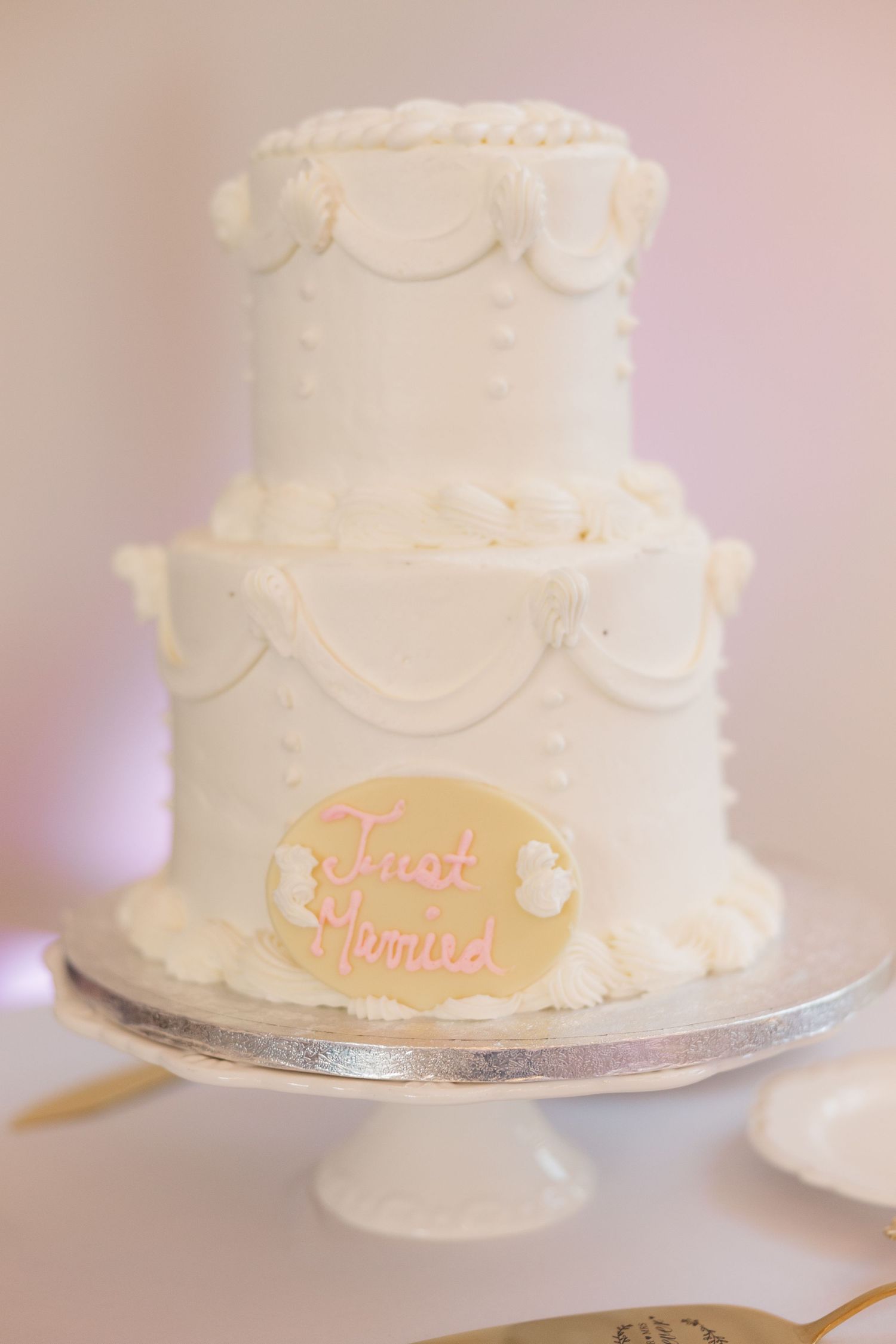 White two-tier wedding cake with delicate piping and 'Just Married' text in pink.