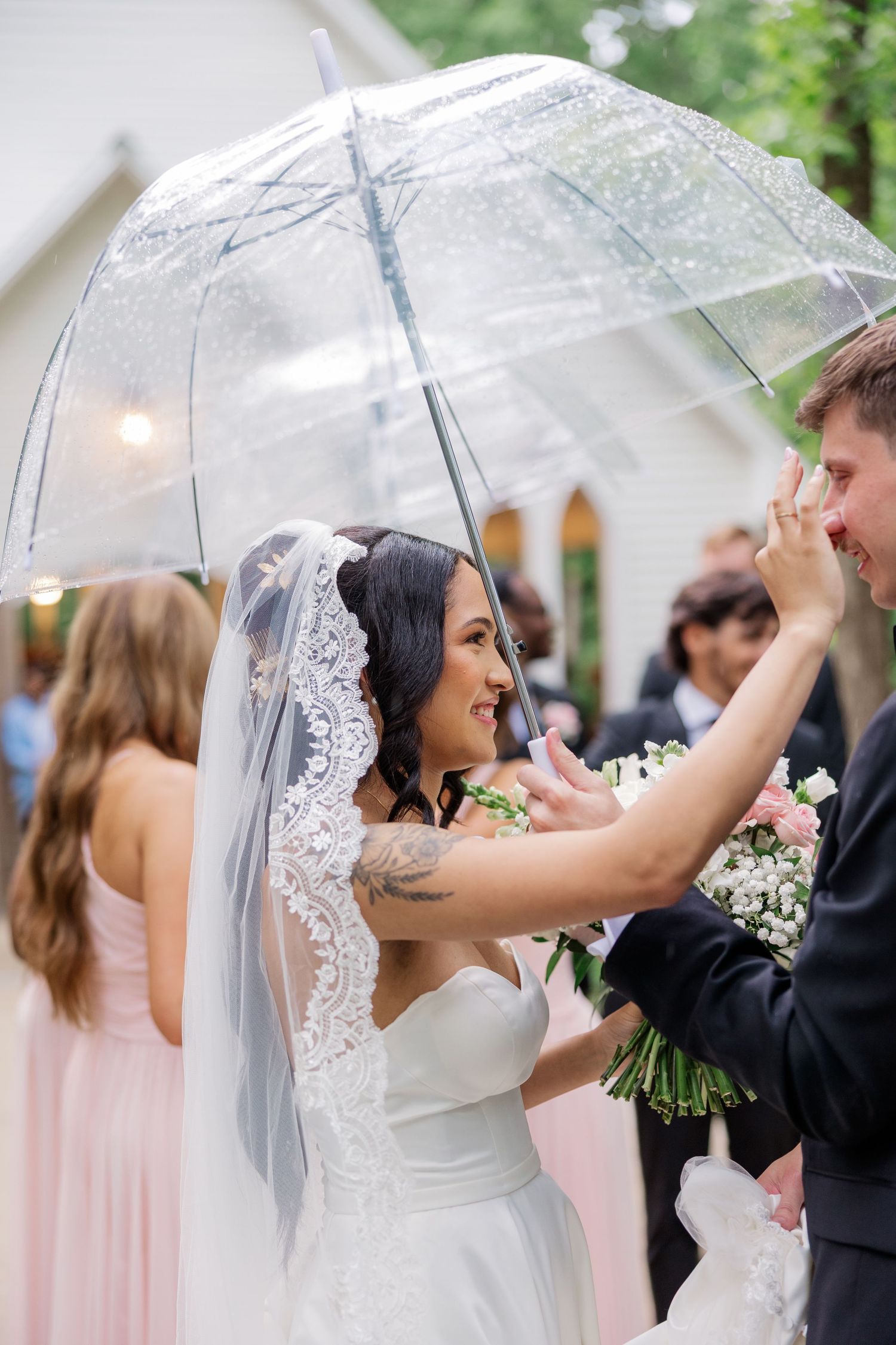 Clear umbrella adds whimsy to an outdoor wedding celebration with pink bridesmaid dresses.