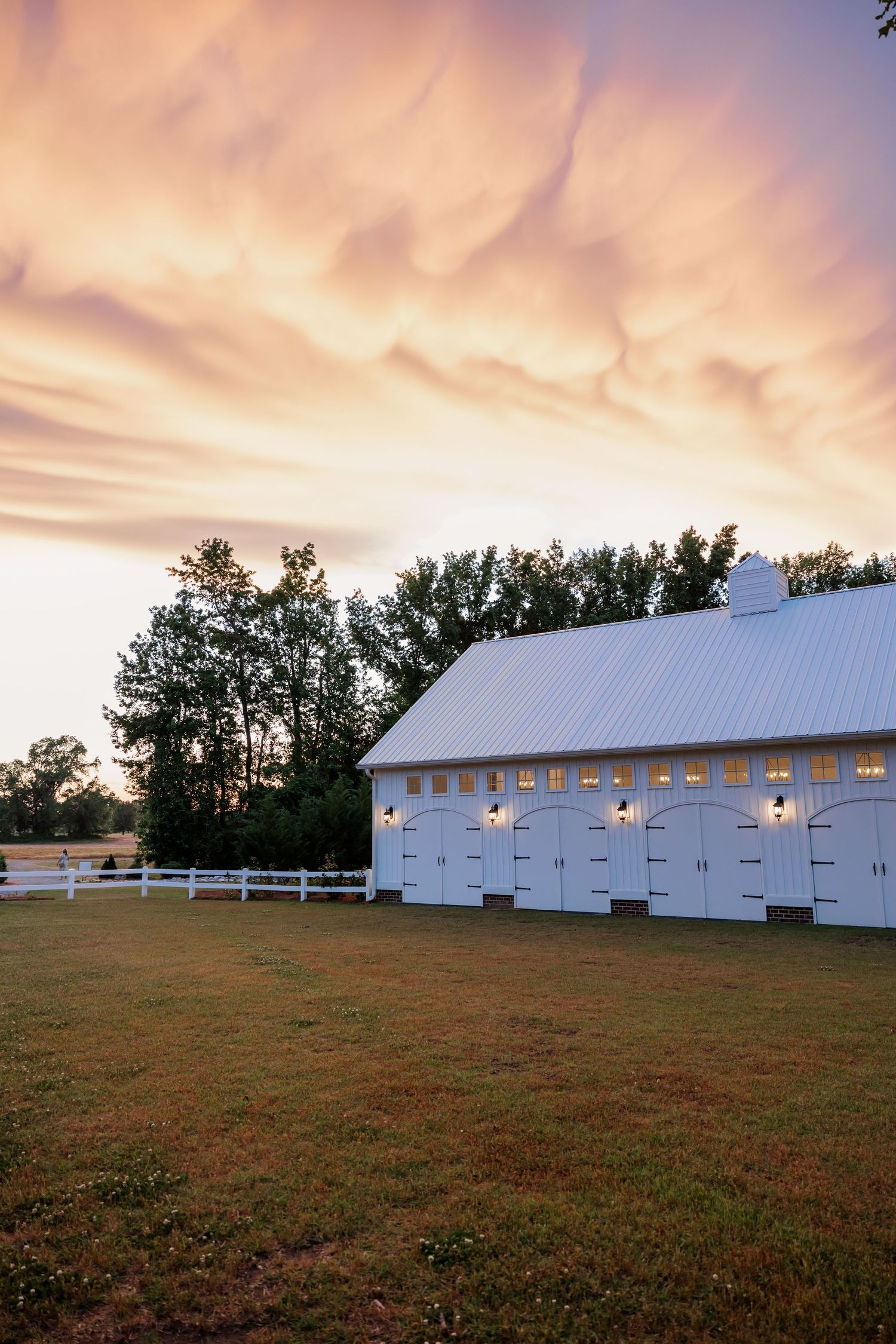 A white modern barn wedding venue at sunset with a dramatic pink and orange sky.
