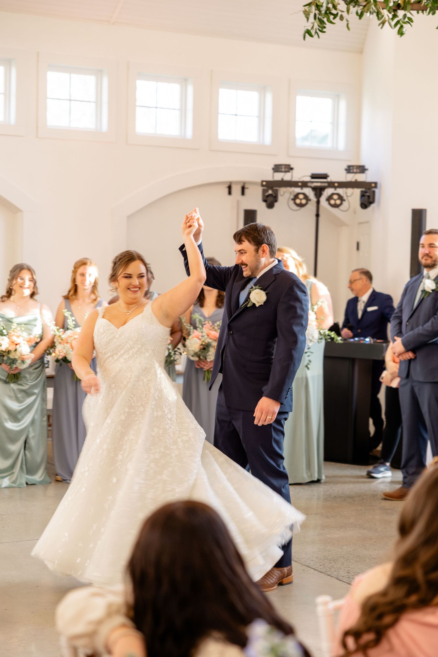 Wedding party dancing and celebrating in a bright modern reception venue with high ceilings.