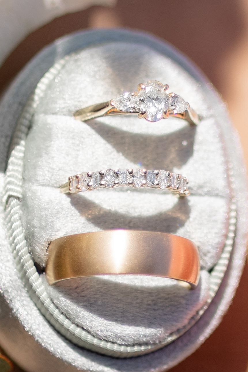 Three wedding rings including a diamond engagement ring, pave band, and plain rose gold band nestled in a light gray ring box.