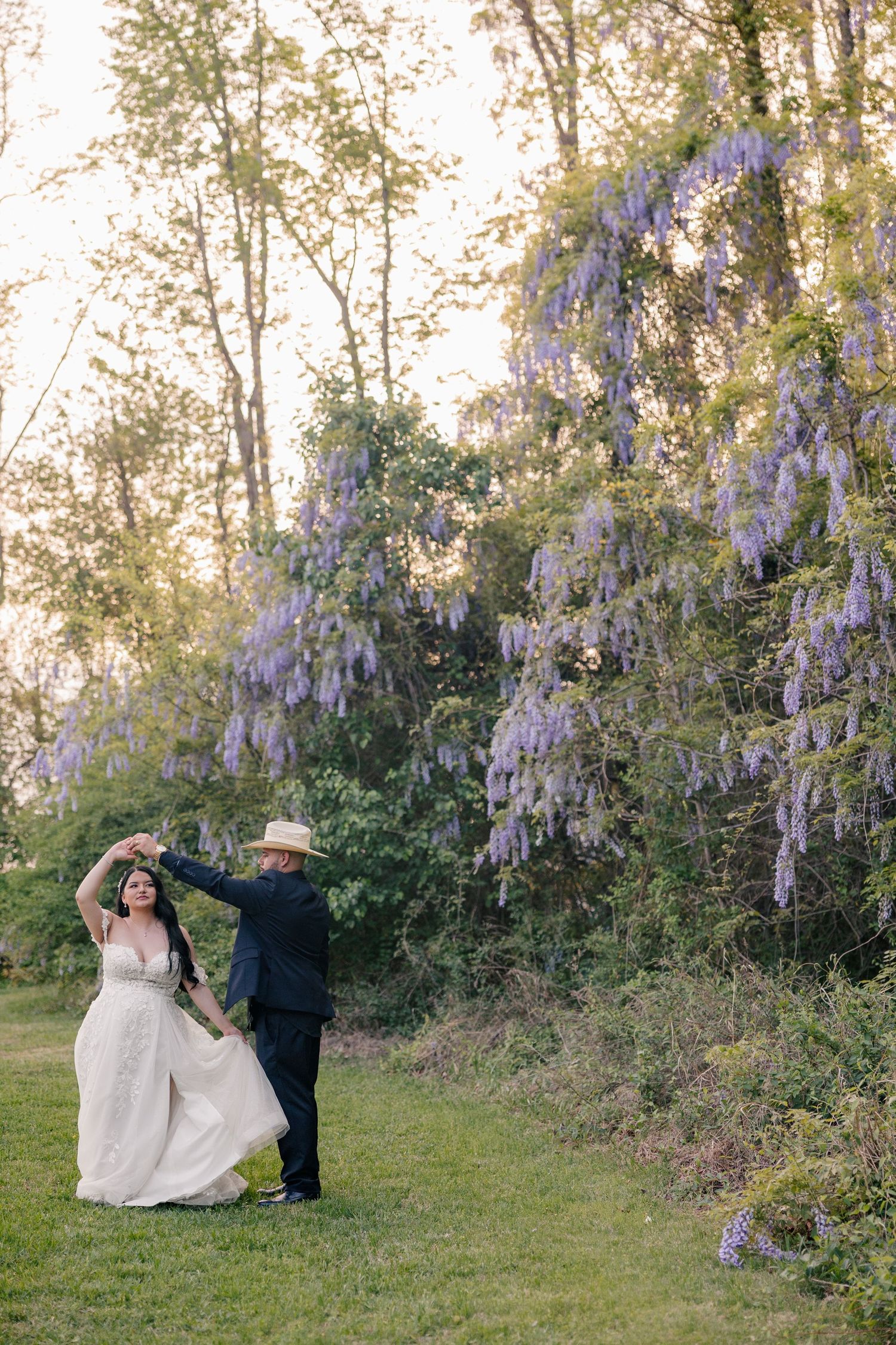 Romantic wedding portraits captured among blooming wisteria vines in garden setting.