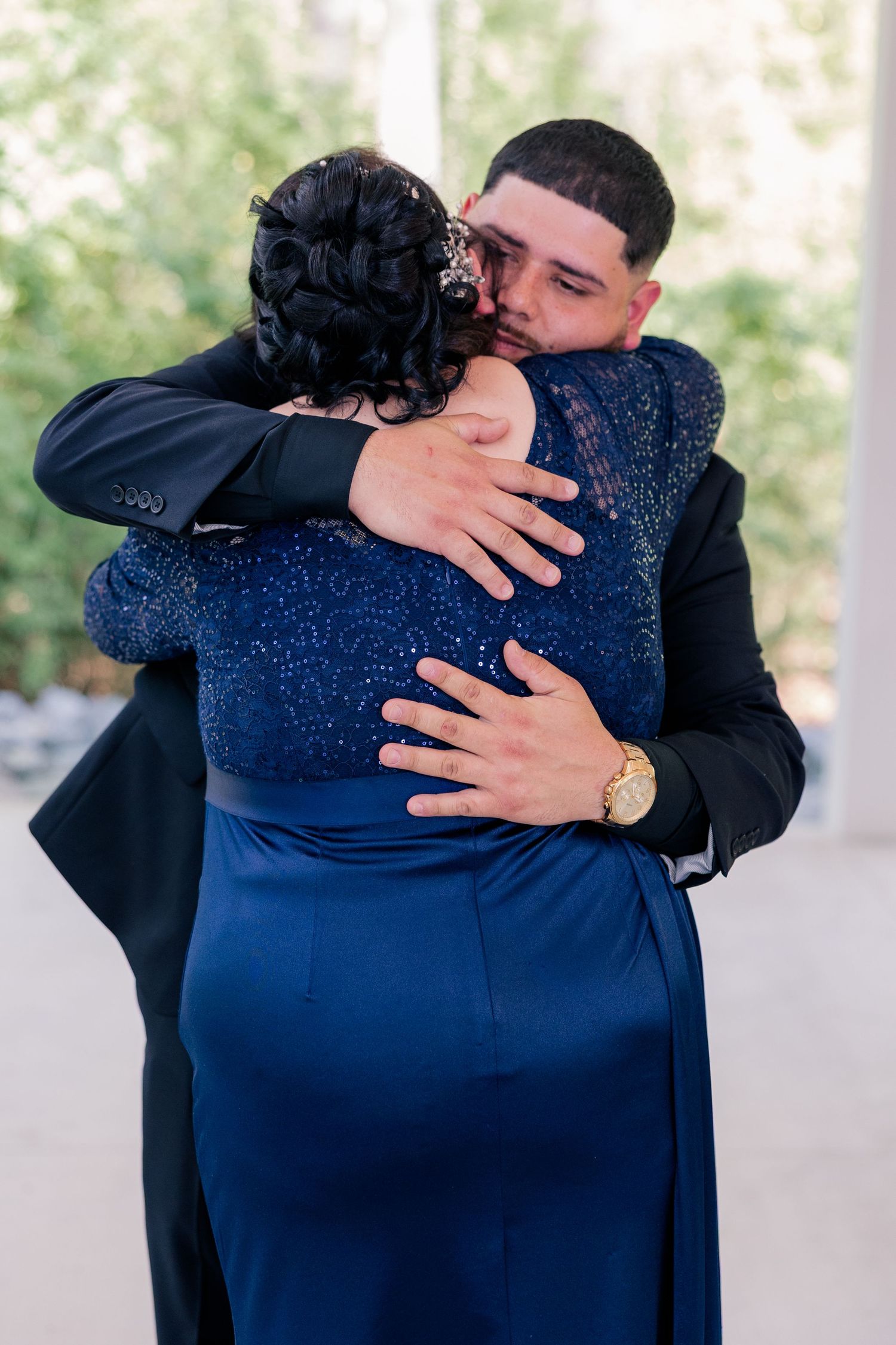 An emotional embrace between two people, one wearing a navy blue gown and the other in a black suit.