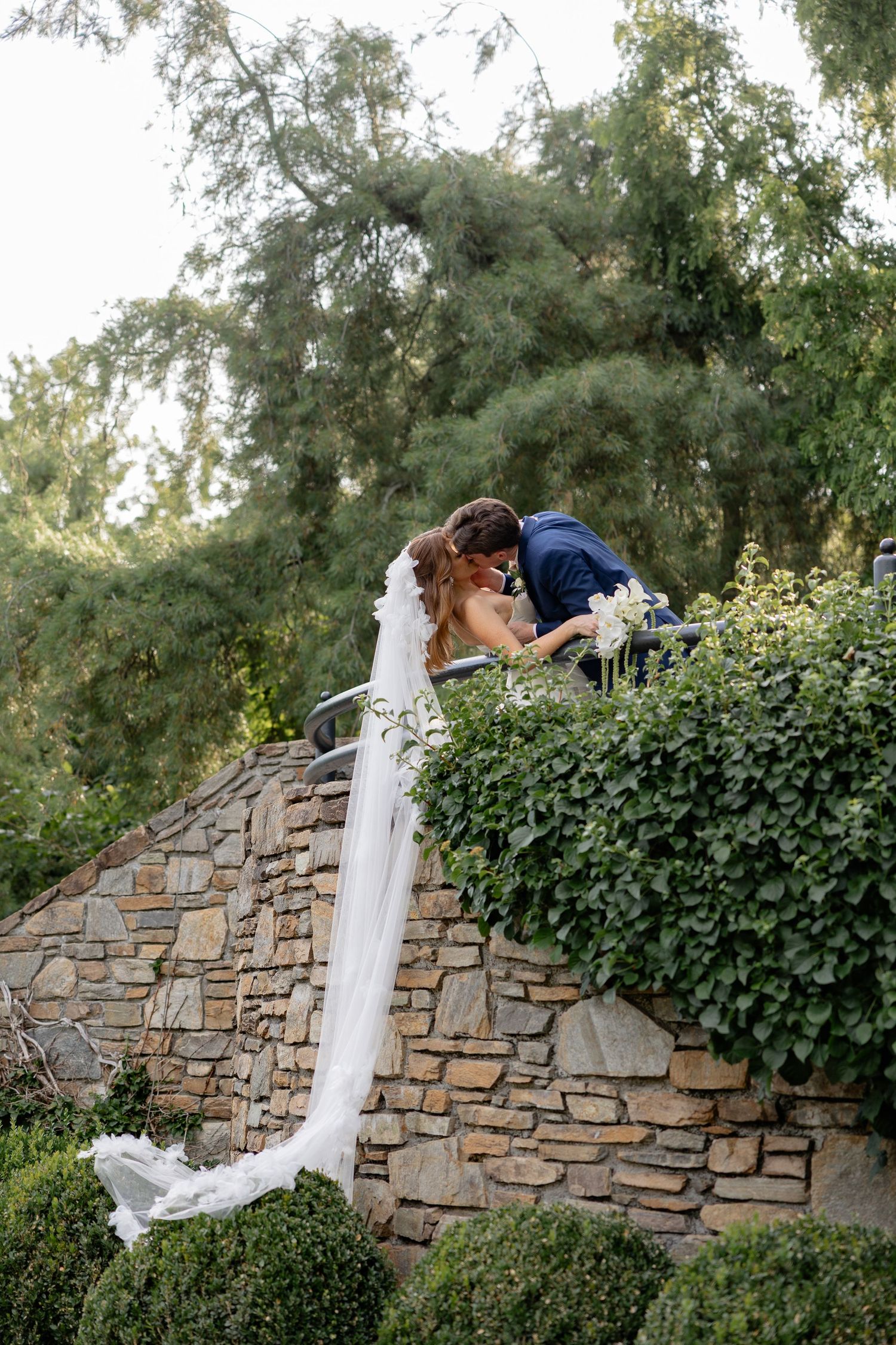 A romantic moment captured on a stone wall surrounded by lush greenery.