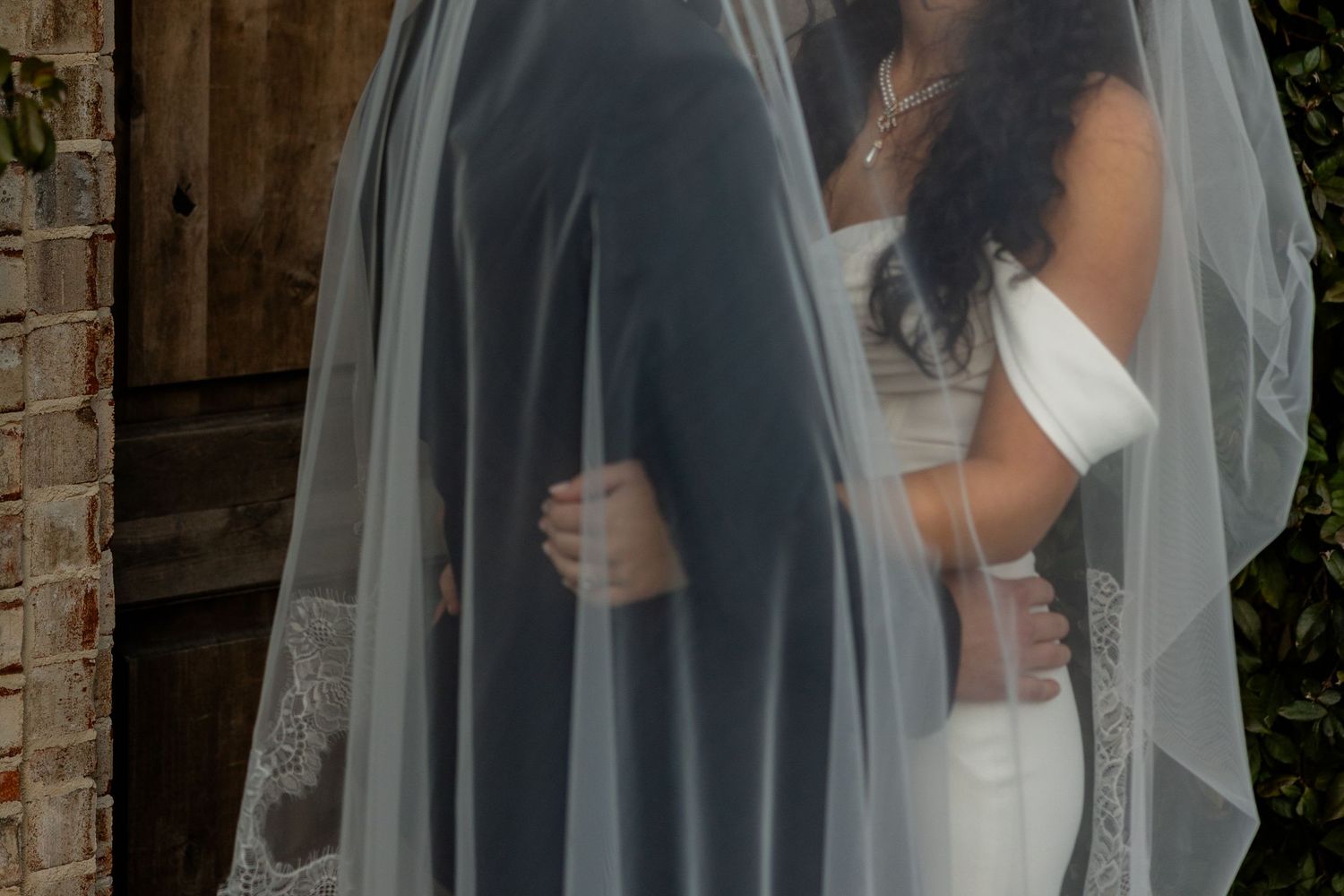 Close-up detail of bride and groom embracing through delicate wedding veil.