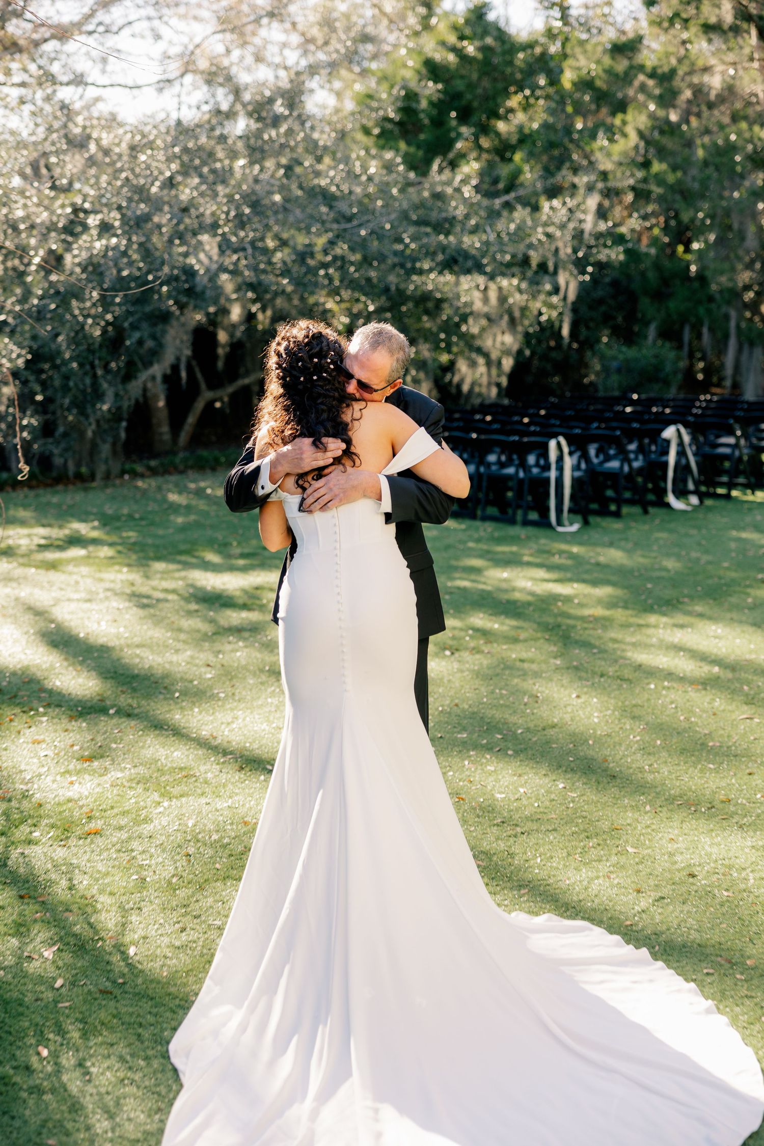 A couple embraces in a romantic moment on their wedding day in a sunlit garden setting.
