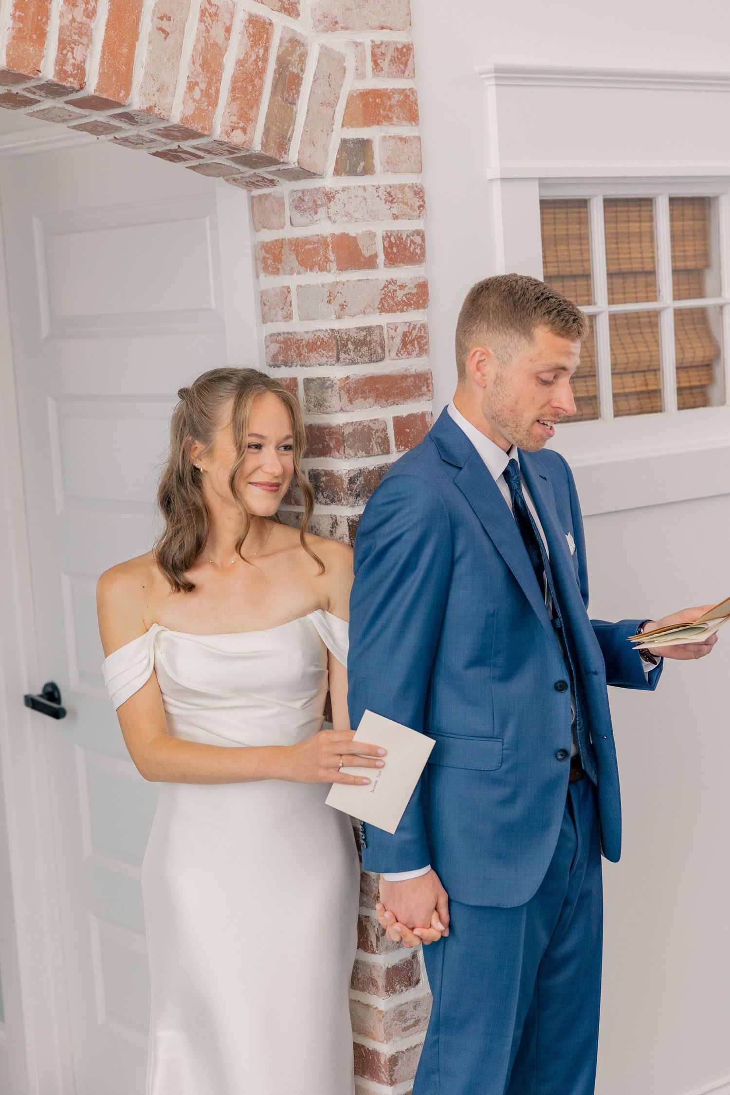 Bride and groom share private vows back-to-back holding hands through doorway before wedding ceremony.