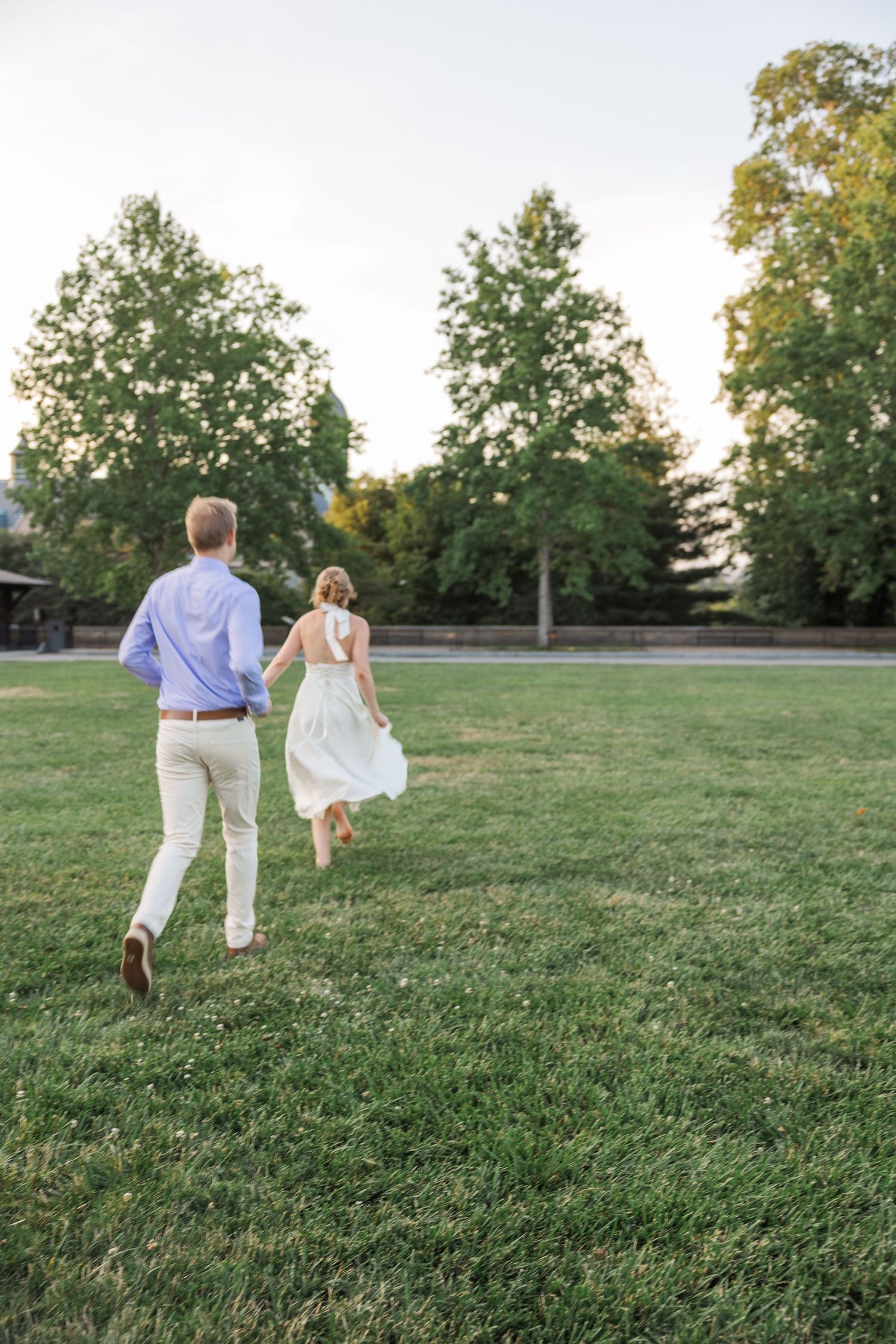 A couple runs playfully across a green lawn during a summer evening photoshoot.