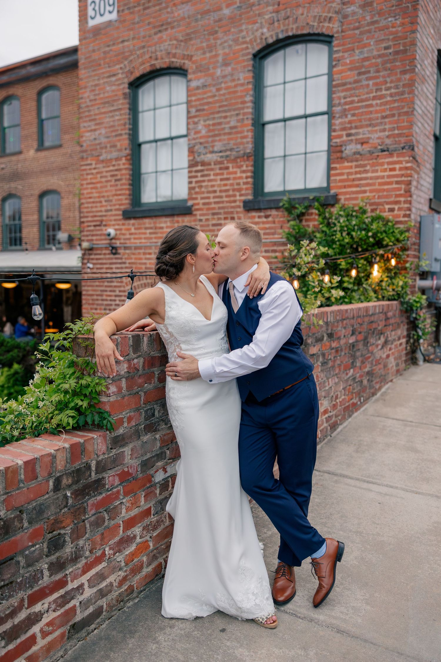 Bride and groom share a kiss outside a historic brick building on their wedding day.