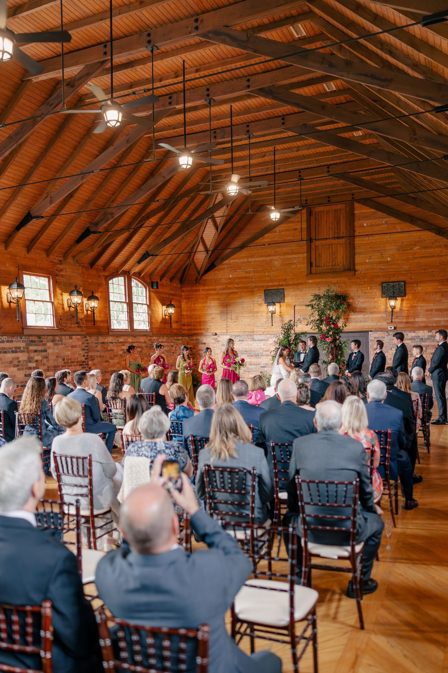 Wedding ceremony inside rustic wooden barn venue with guests seated in chiavari chairs.