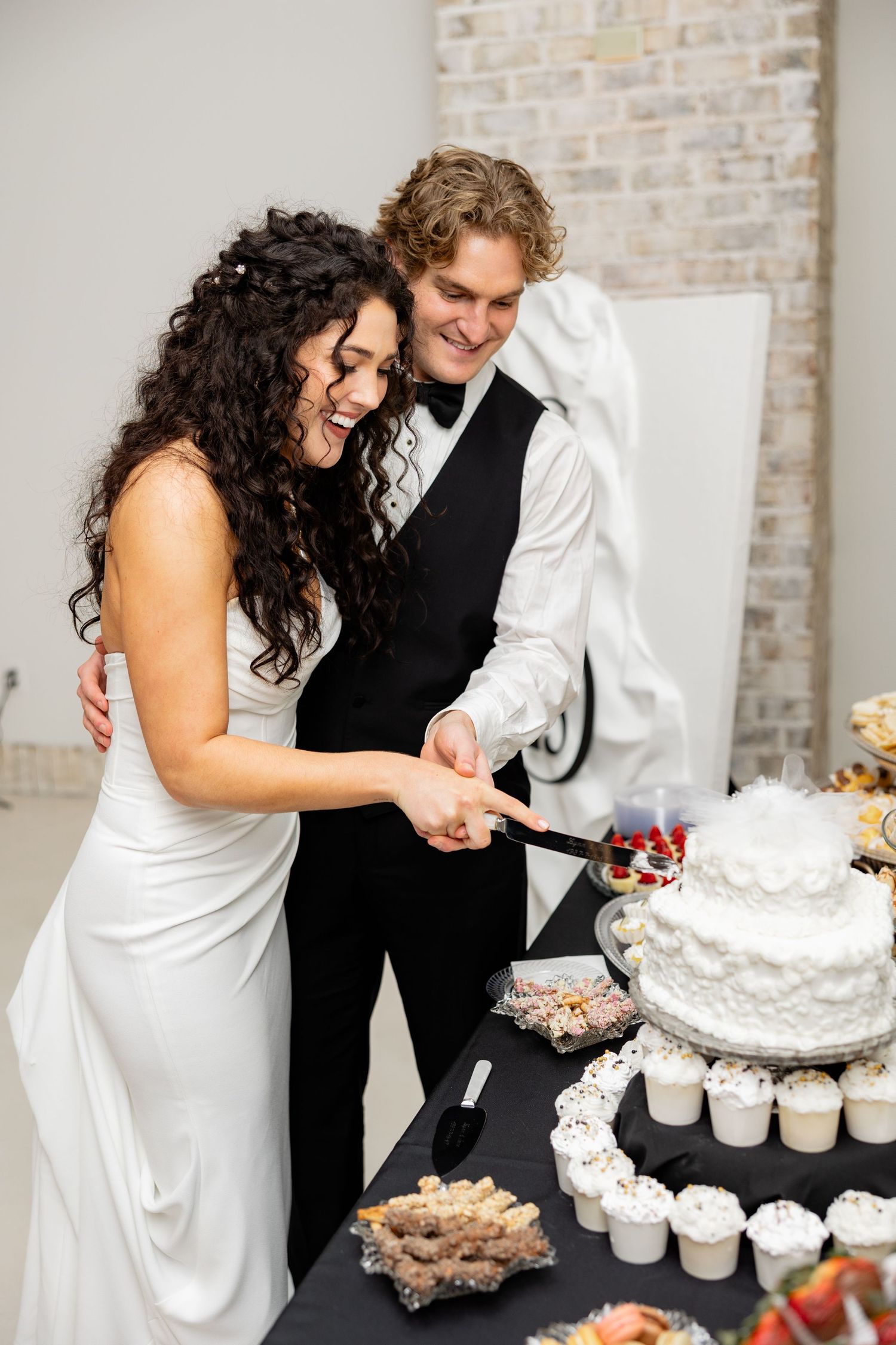 Newlyweds share a joyful moment while cutting their white wedding cake at the reception.