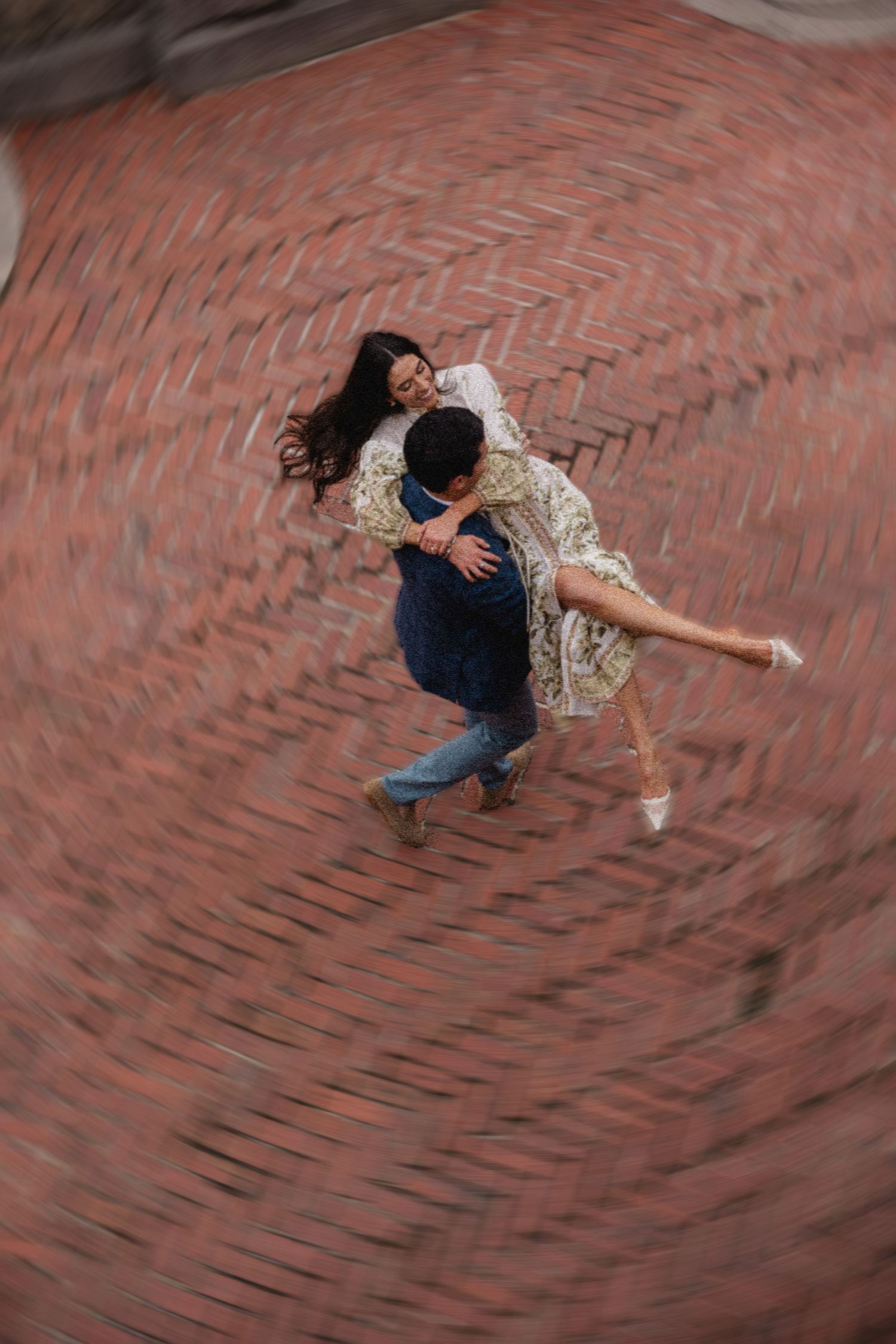 A couple dancing and spinning on brick pavement captured with motion blur effect from above.