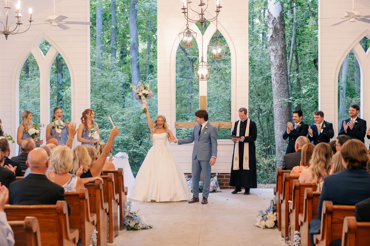 Bride and groom celebrate at the altar of a stunning glass chapel surrounded by lush trees during their wedding ceremony.