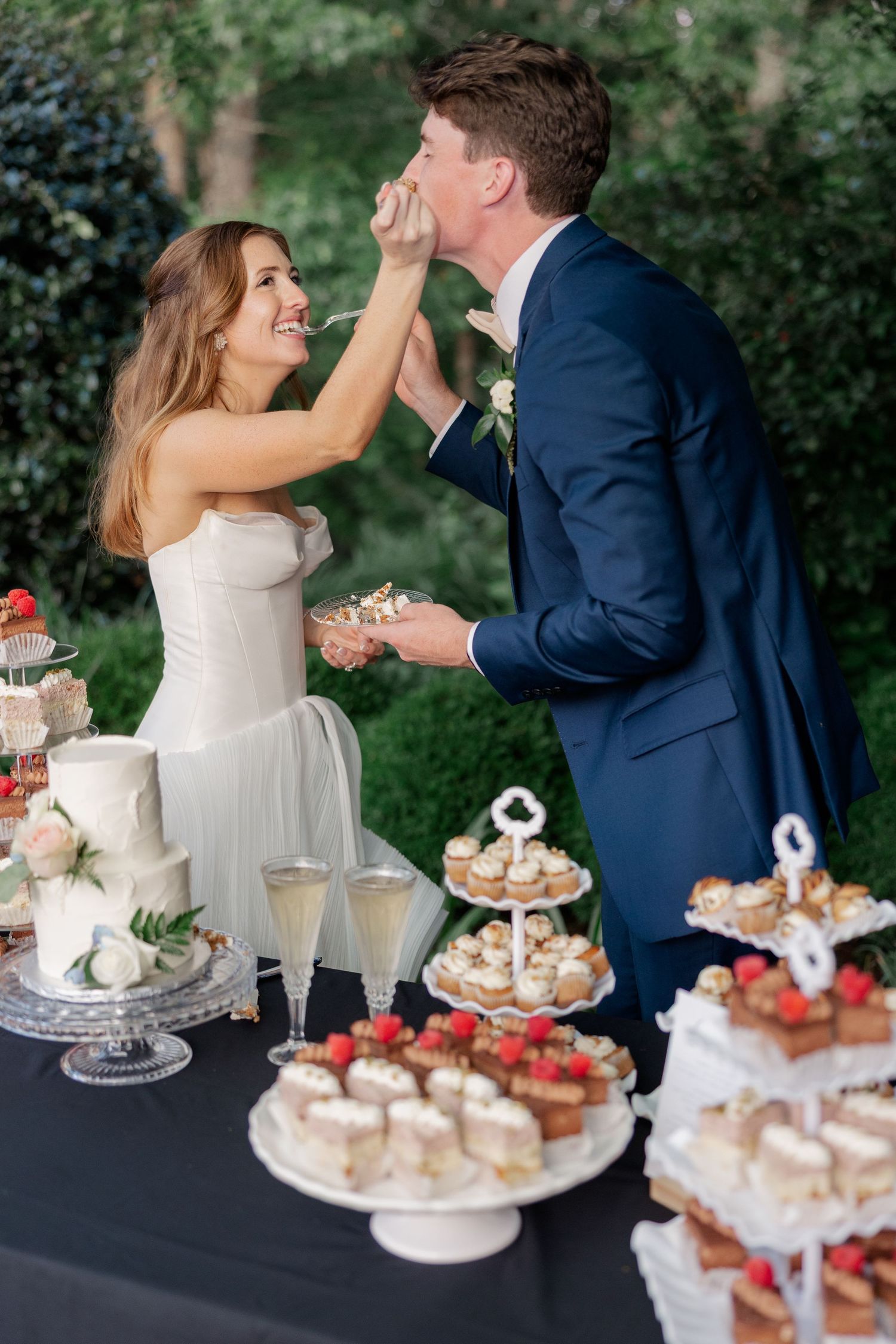 Wedding couple sharing desserts and cake at an outdoor reception table.