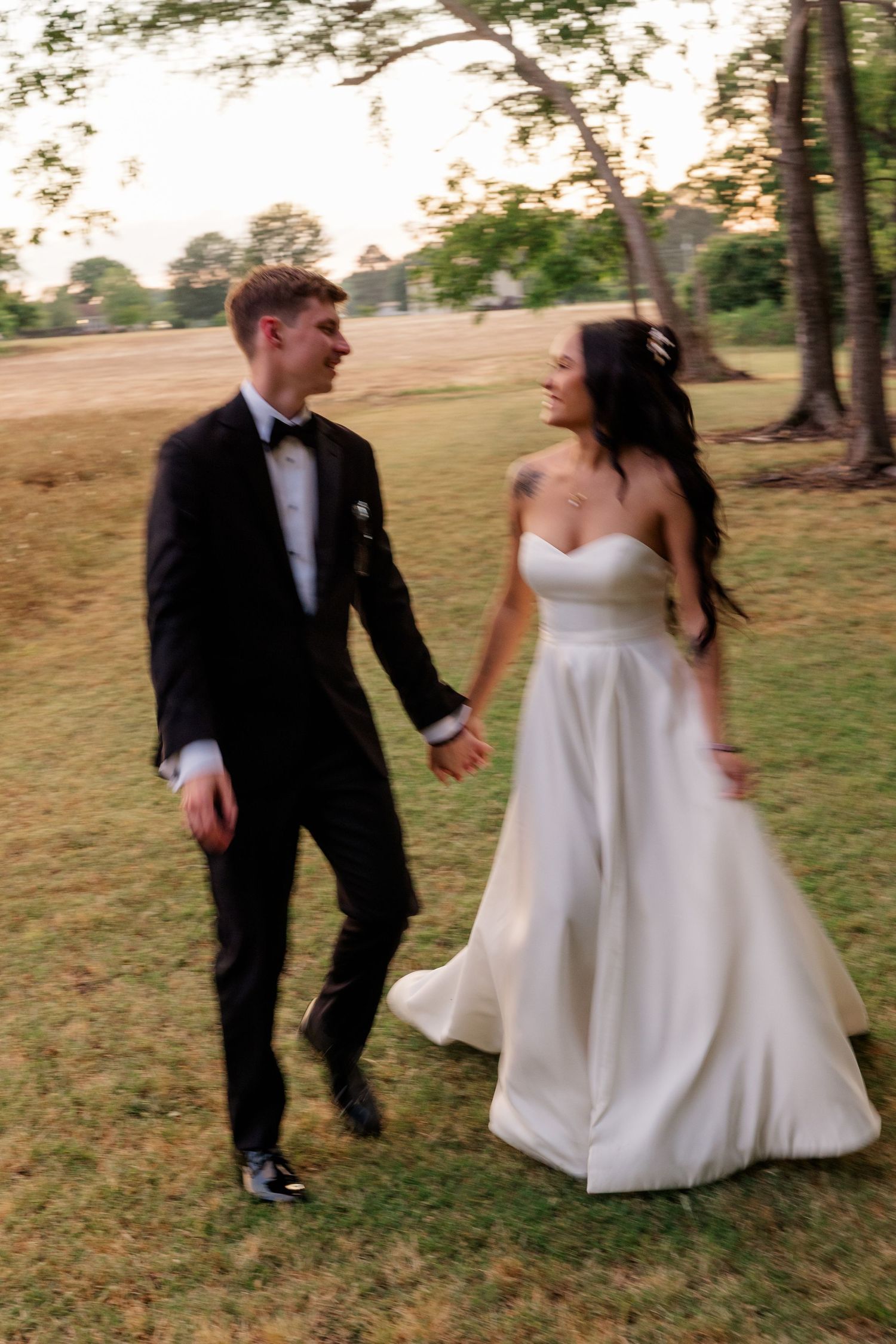 Playful bride and groom running through a grassy field during their wedding photoshoot.