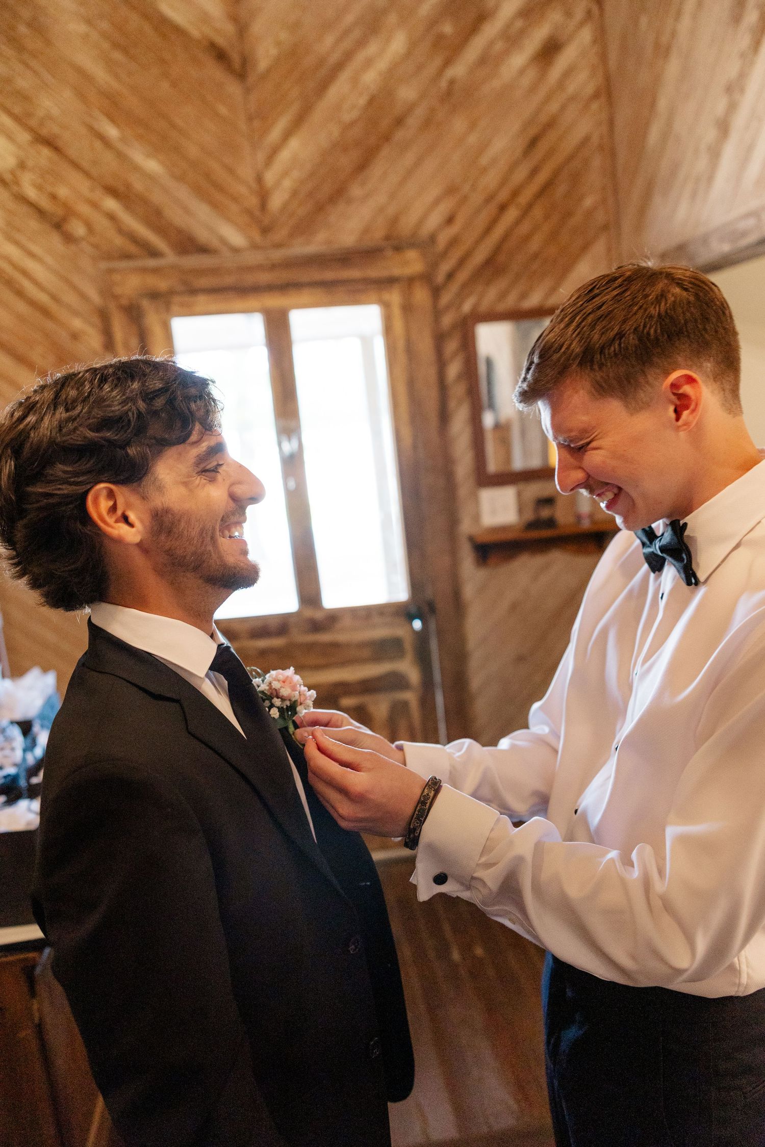 A boutonniere is being pinned onto a suit lapel in a rustic wooden interior setting.