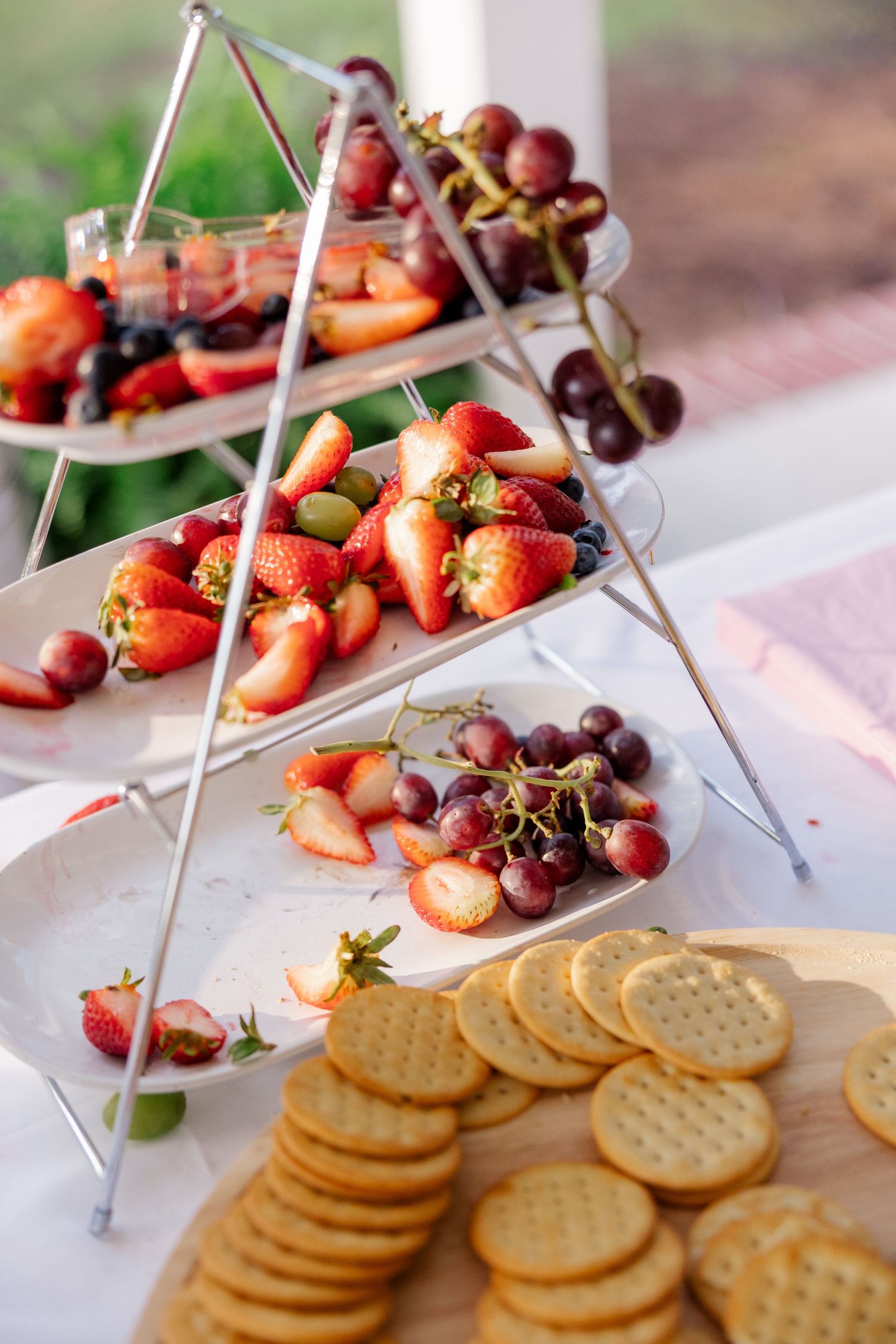 Elegant tiered display of fresh strawberries, grapes and butter crackers arranged on white serving platters.