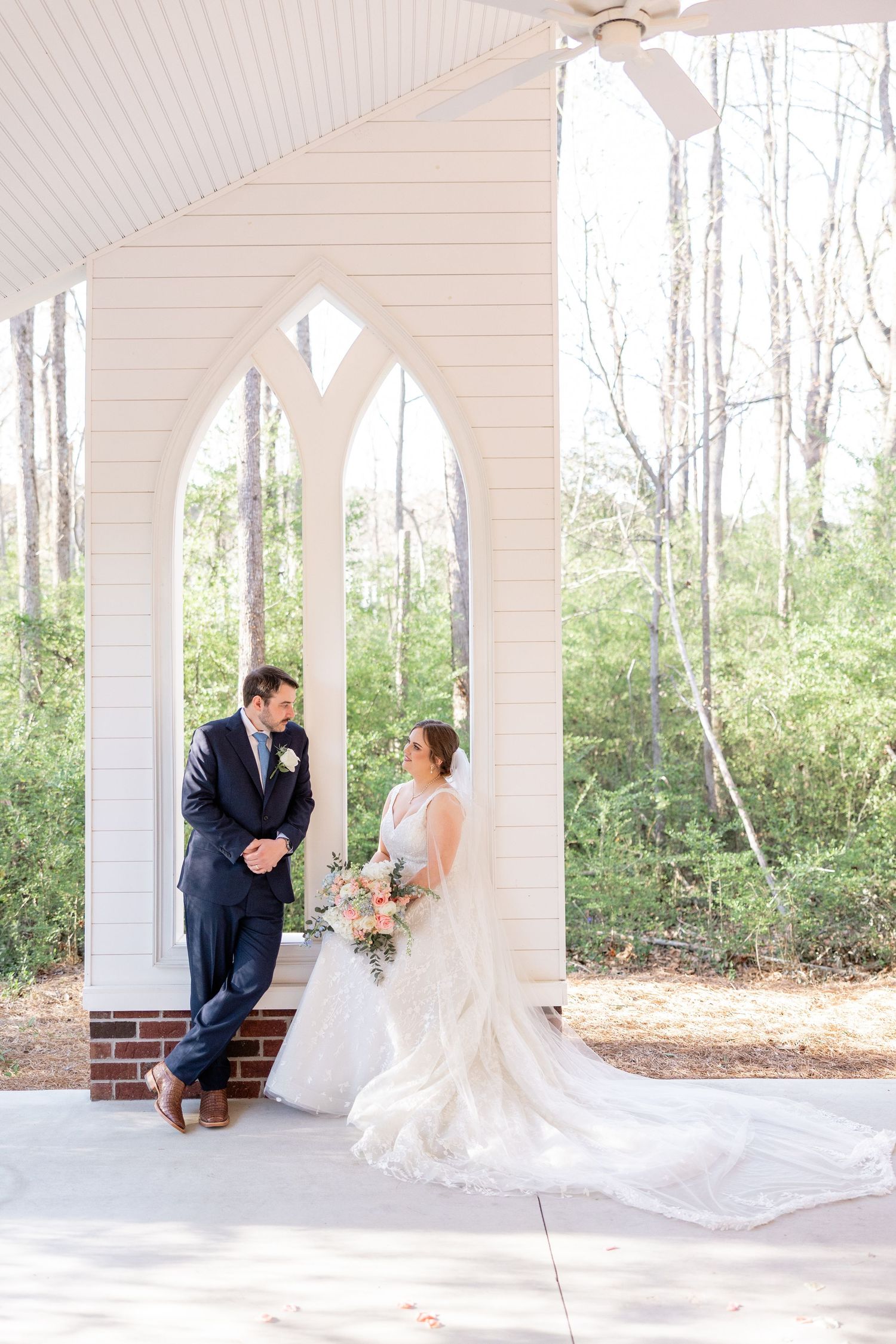 Wedding couple shares intimate moment on white columned porch surrounded by trees.