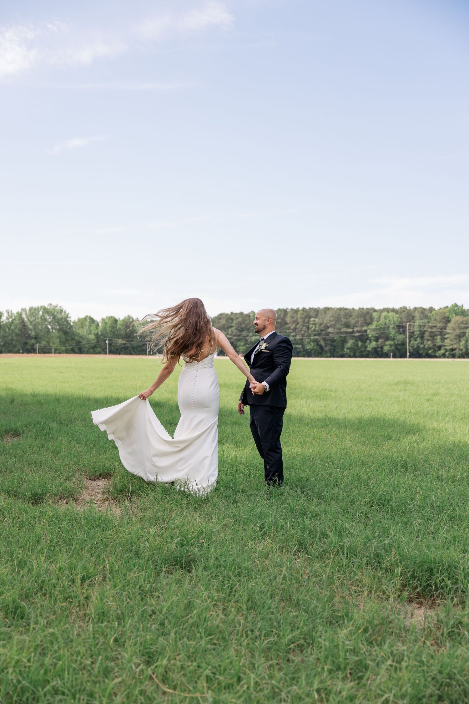 Bride's dress flows dramatically in the wind during outdoor wedding photos in an open field.