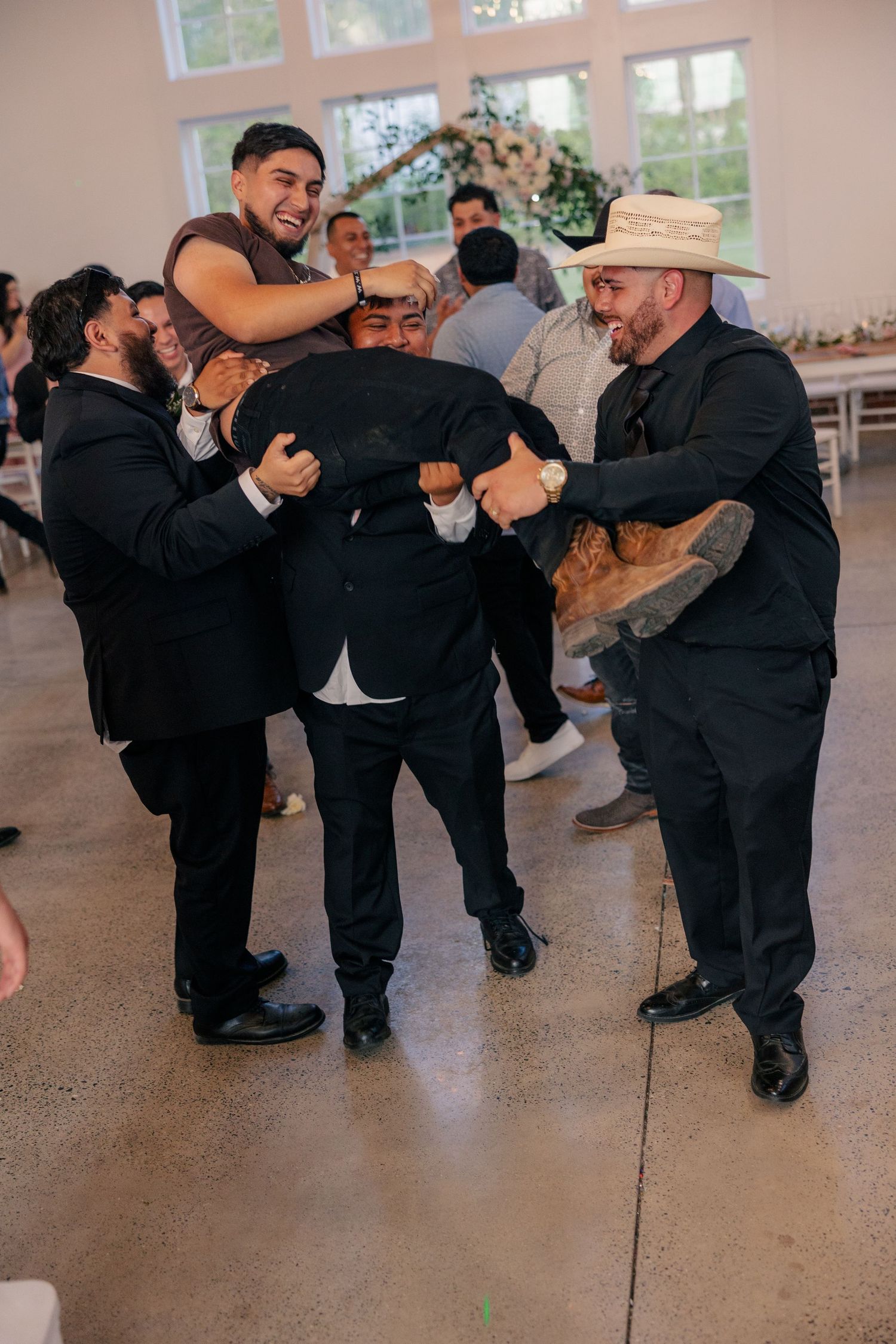 Groomsmen in black suits perform a coordinated dance routine at a wedding reception.