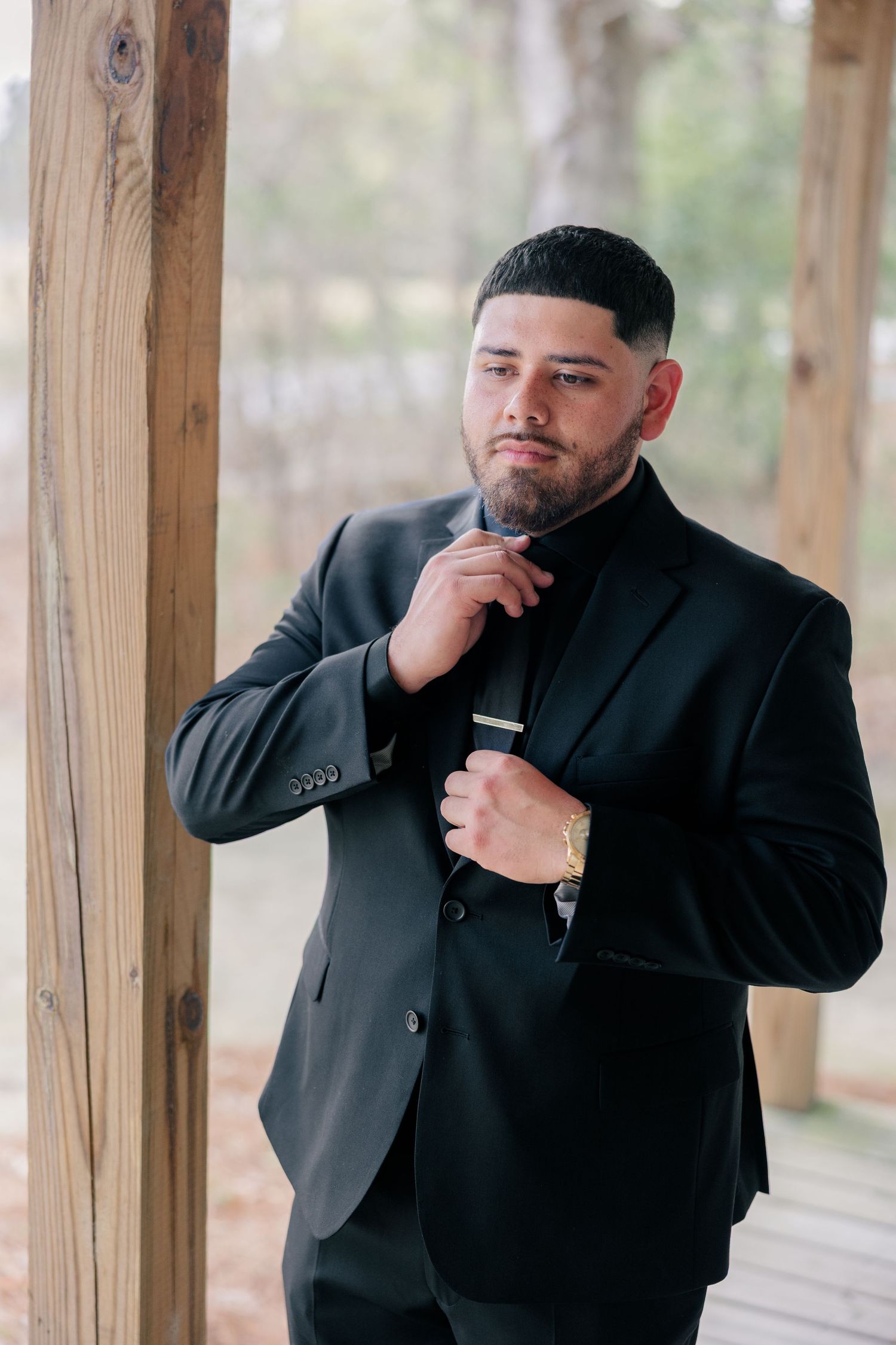 Someone in a black suit poses thoughtfully in a wooden covered porch.