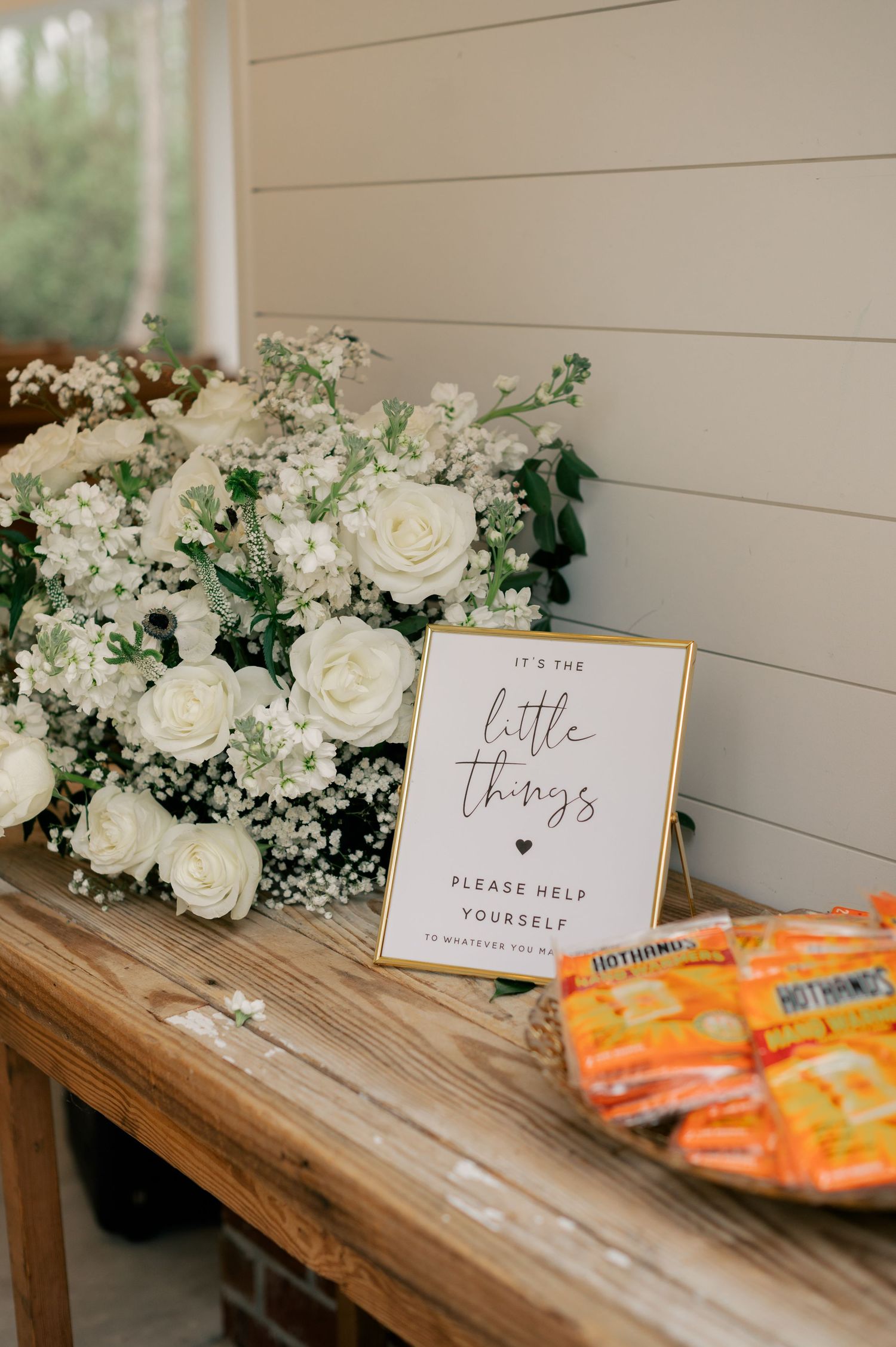 White roses and baby's breath arrangement with a wedding sign on rustic wooden table.