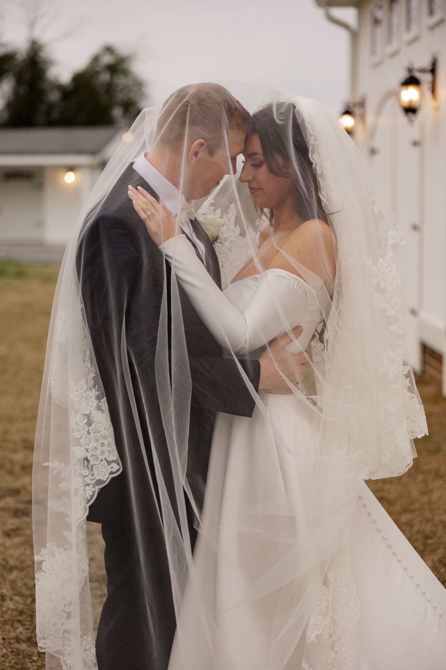 Intimate wedding moment captured outside a white building with string lights and vintage charm.
