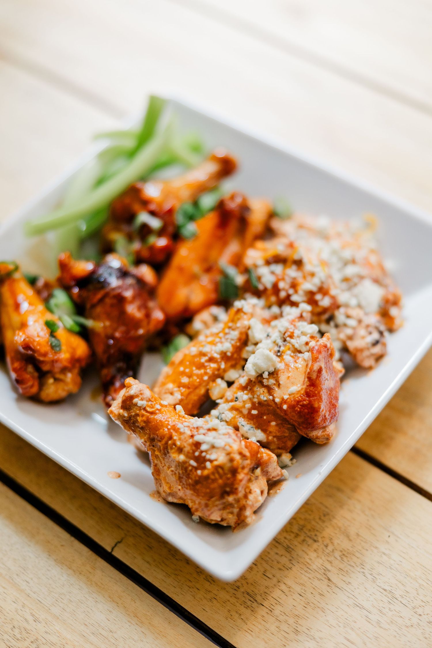 A plate of crispy chicken wings with different sauces and garnishes served on a white square plate on a wooden table.