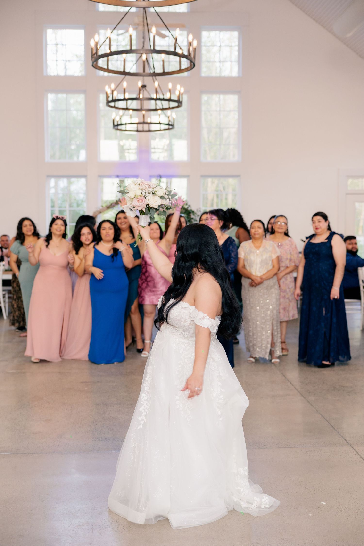 Wedding reception guests dance and celebrate in an elegant white room with chandeliers.