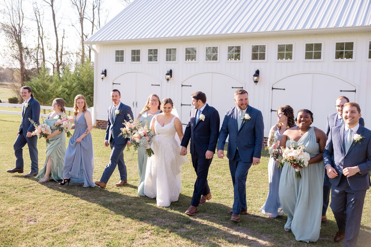 Wedding party lined up for photos outside white building with metal roof.