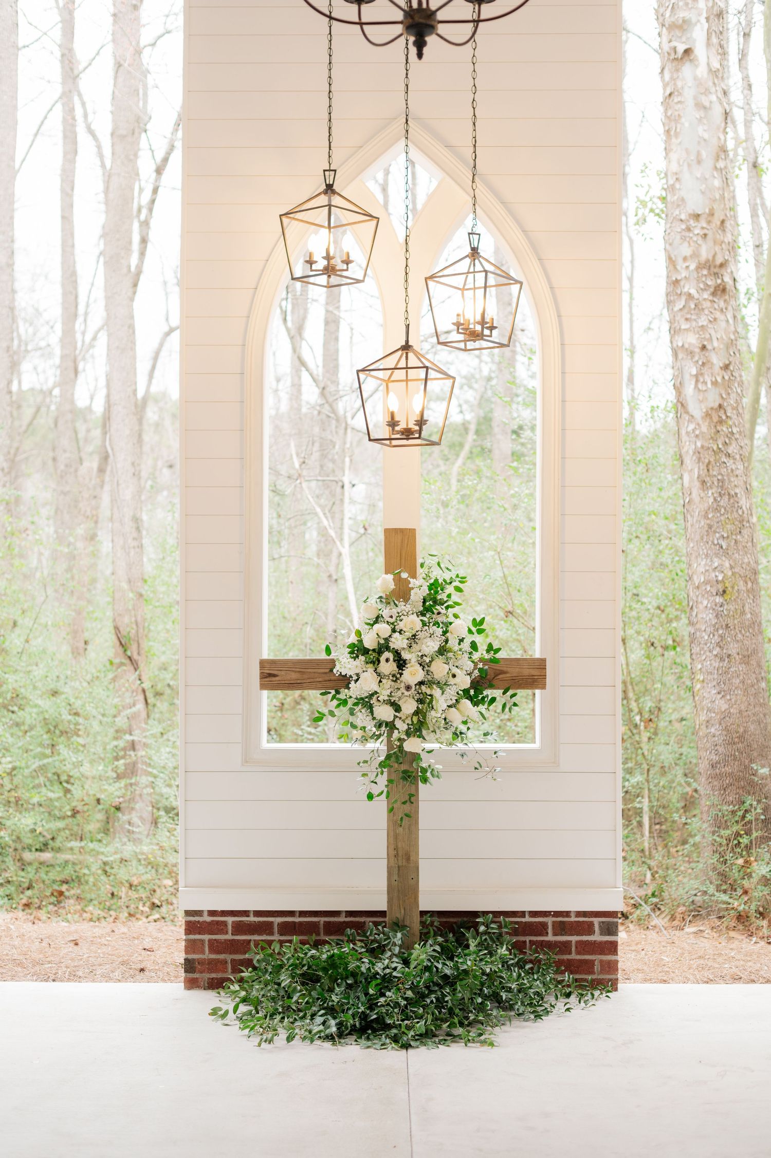 Elegant white chapel interior with hanging lantern lights and floral arrangements against tall windows.